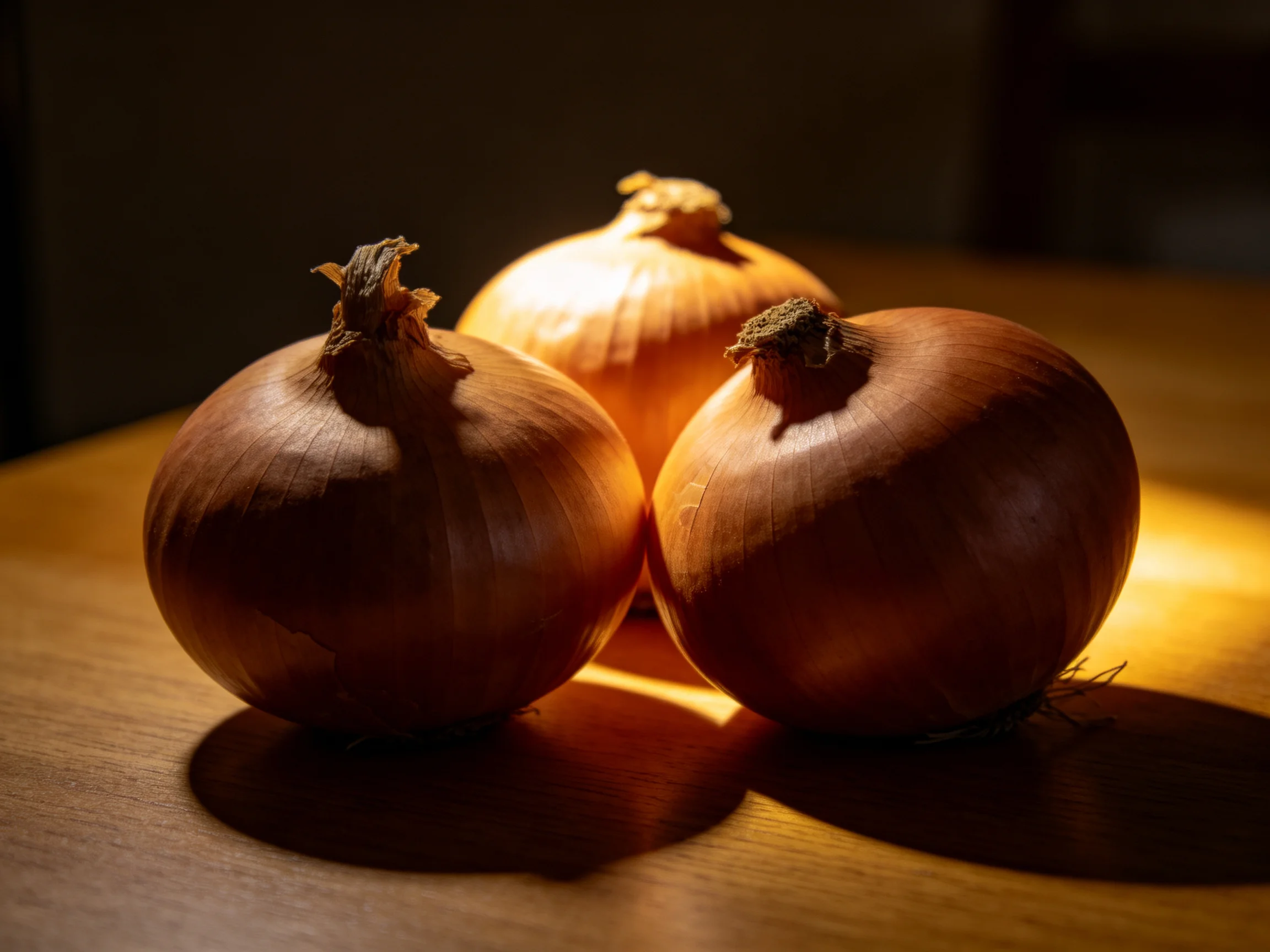 Three golden-brown onions grouped on a wooden surface with dramatic lighting