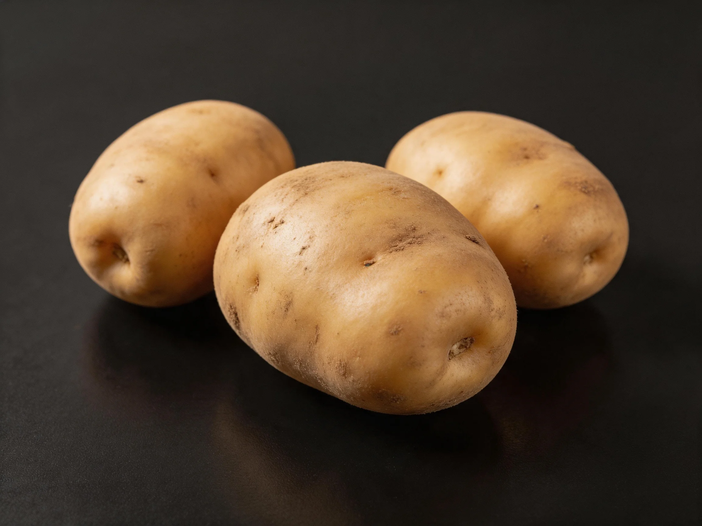 Three light-brown potatoes arranged on a dark surface