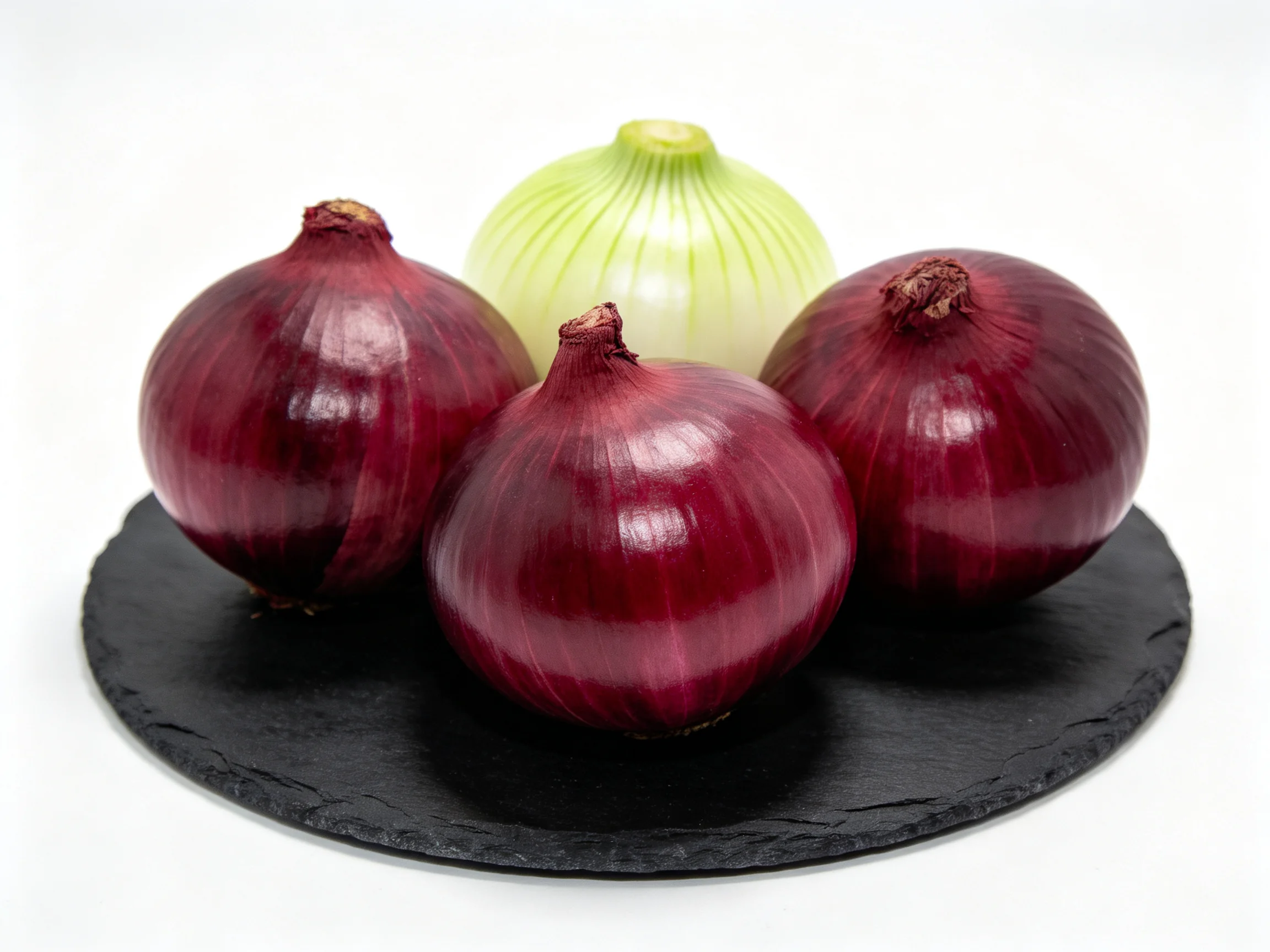 Three red onions and one pale green onion on a dark slate plate