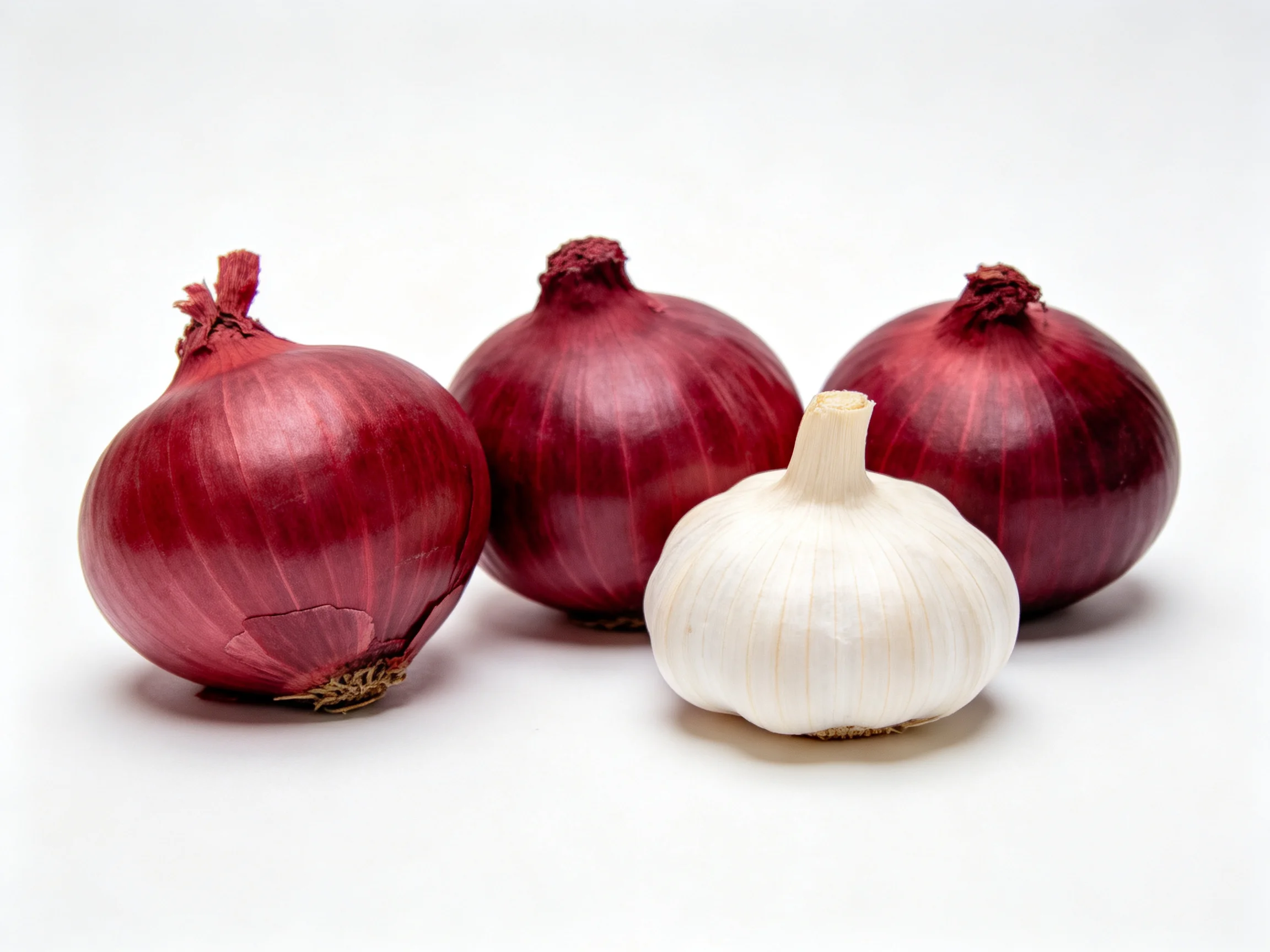 Three red onions and one white garlic bulb arranged on a white surface