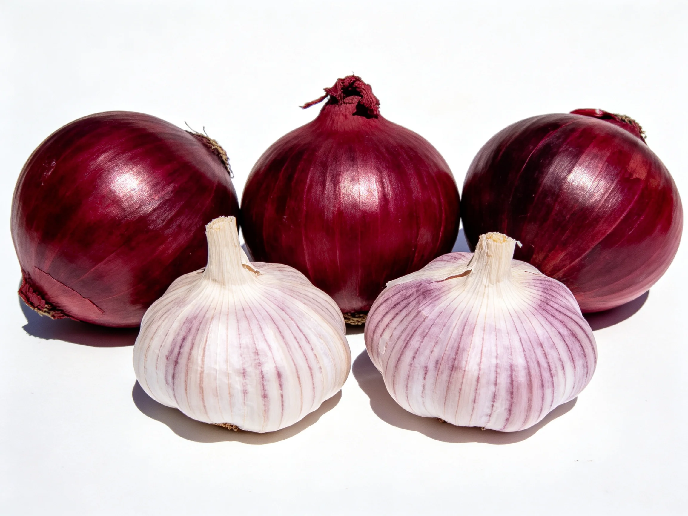 Three red onions and two garlic bulbs displayed on a white surface