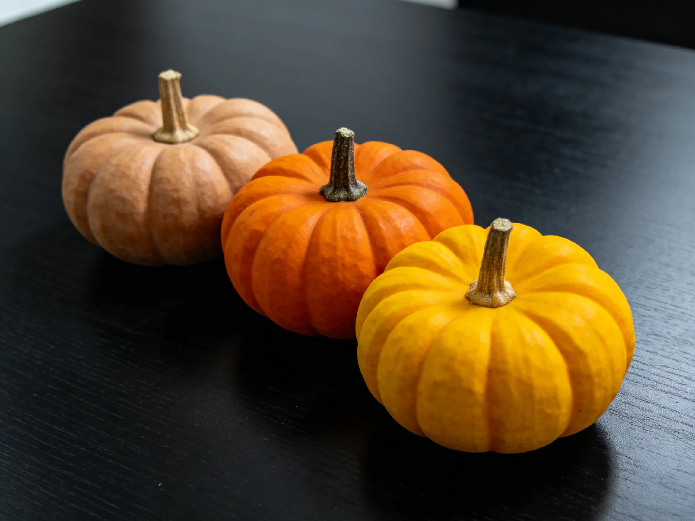 Three small pumpkins in beige, orange, and yellow on a dark wooden table