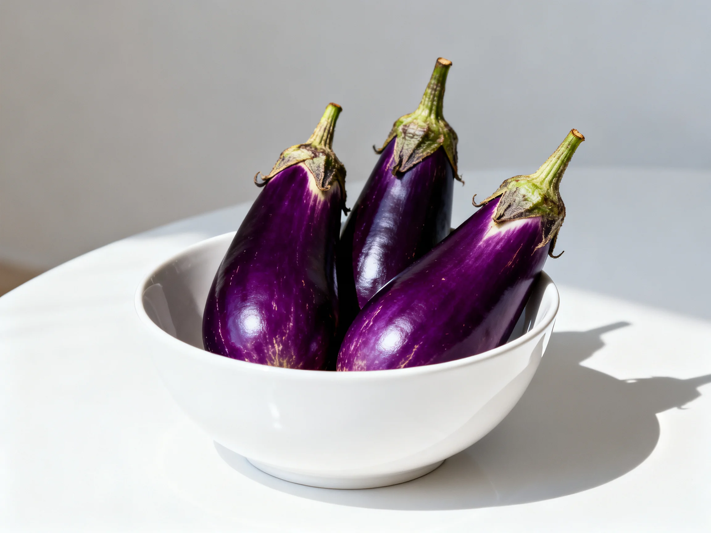 Three vibrant purple eggplants in a white ceramic bowl