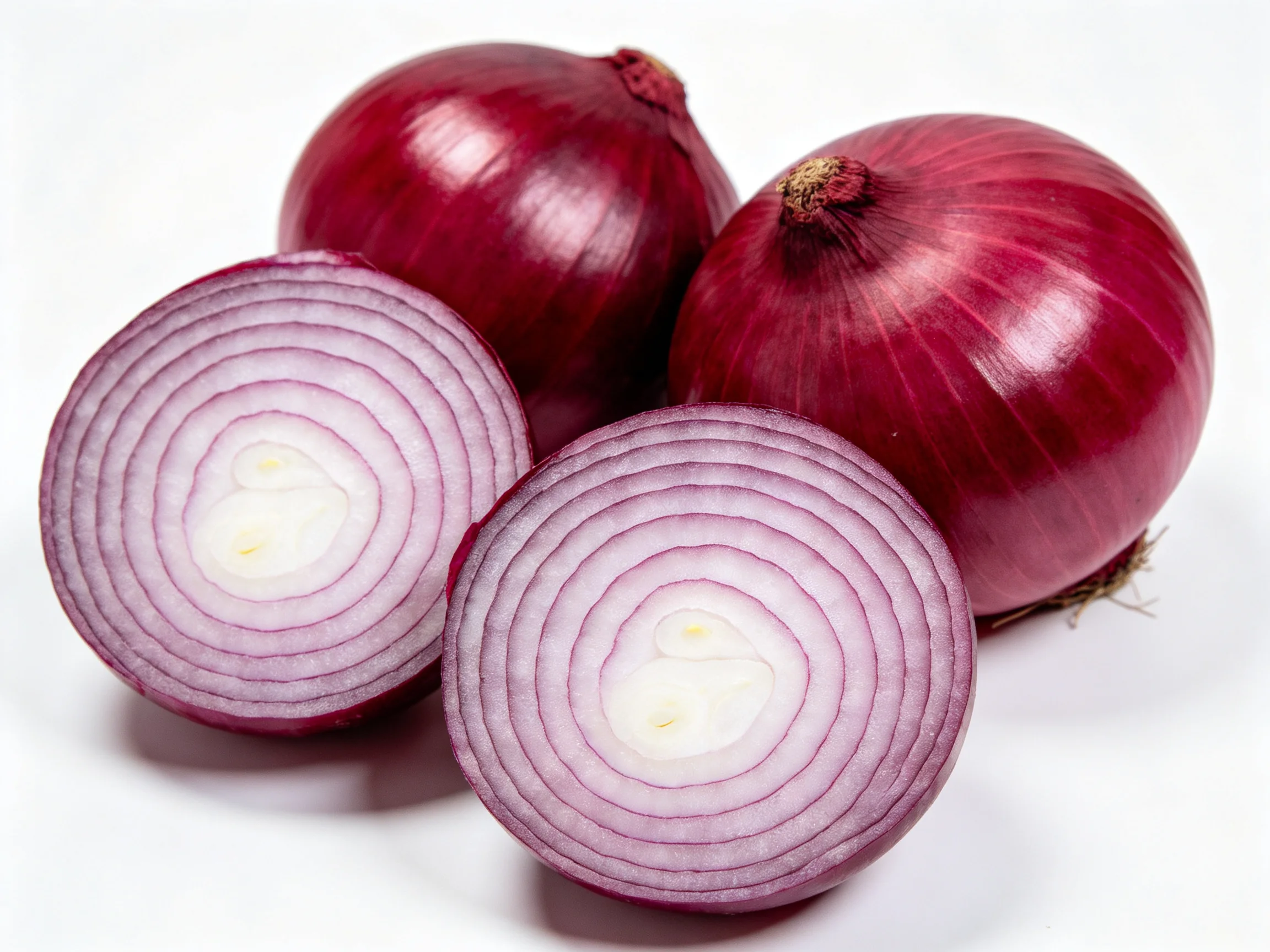 Three whole red onions with two sliced halves showcasing purple concentric rings