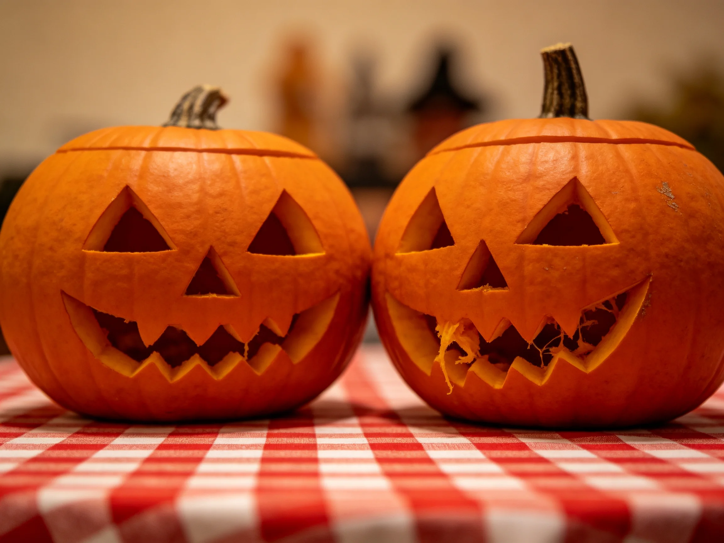 Two carved orange jack-o-lanterns on a red-and-white checkered cloth