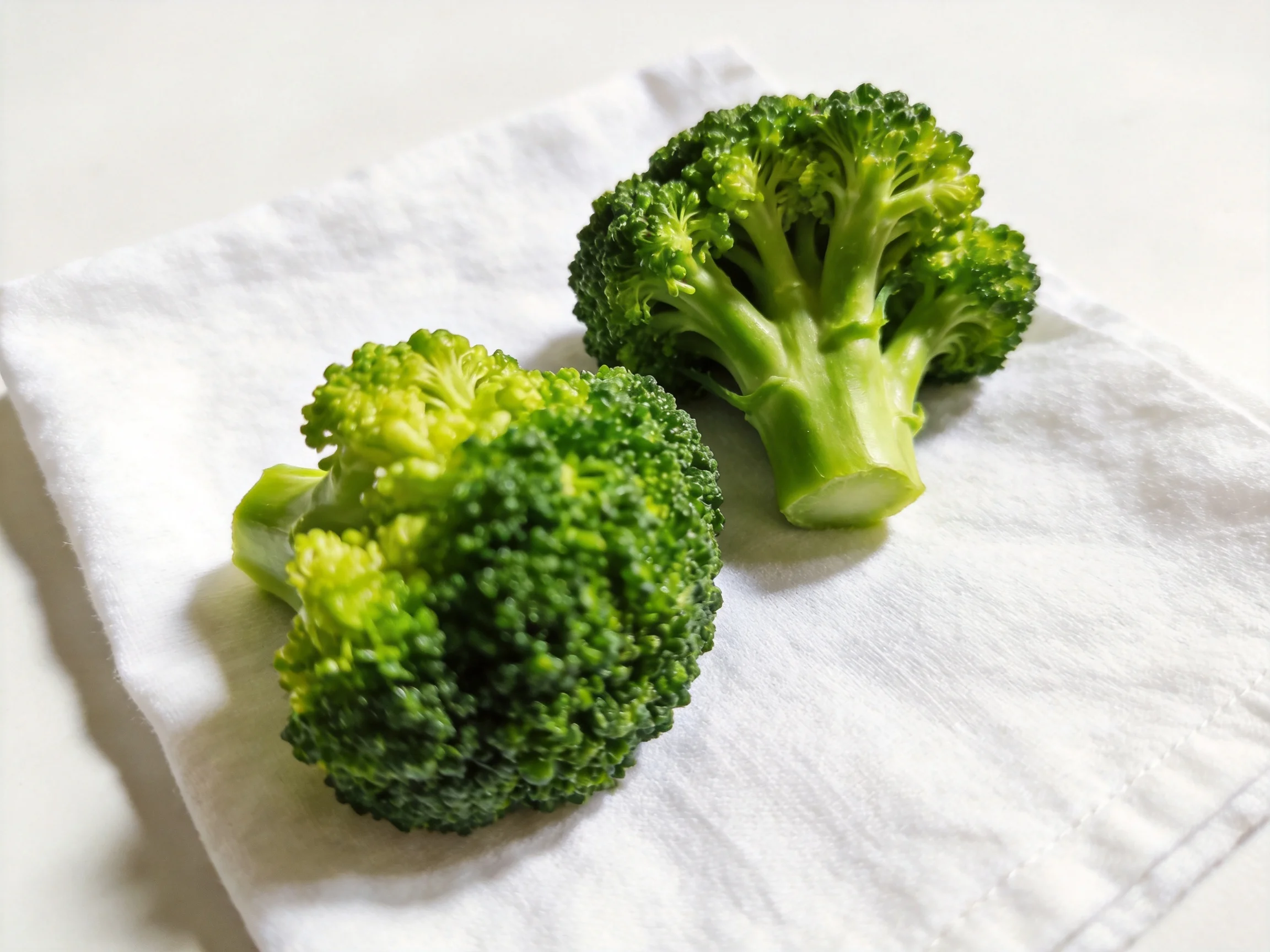 Two fresh green broccoli florets resting on a white cloth