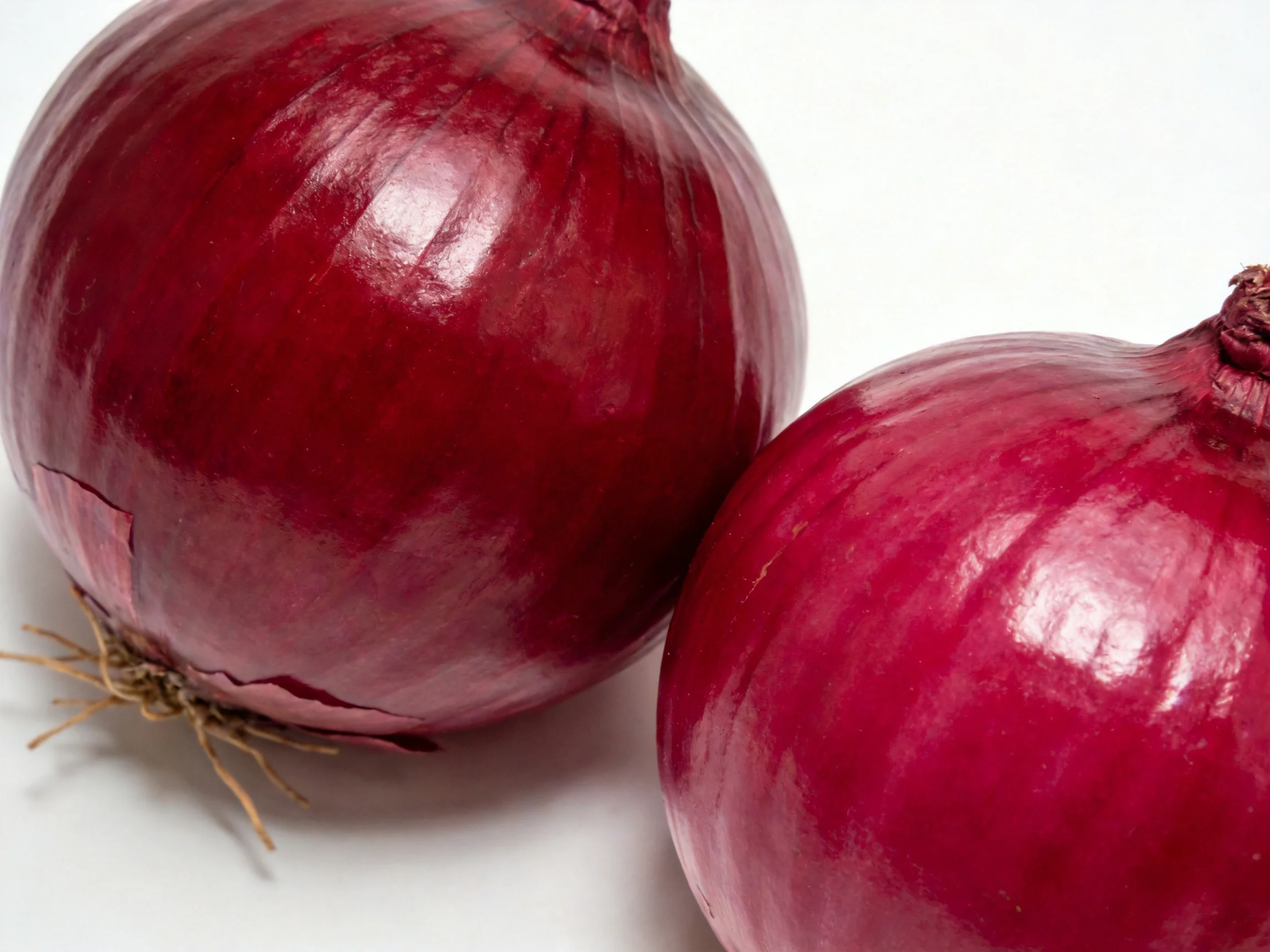 Two glossy red onions displayed on a plain white surface