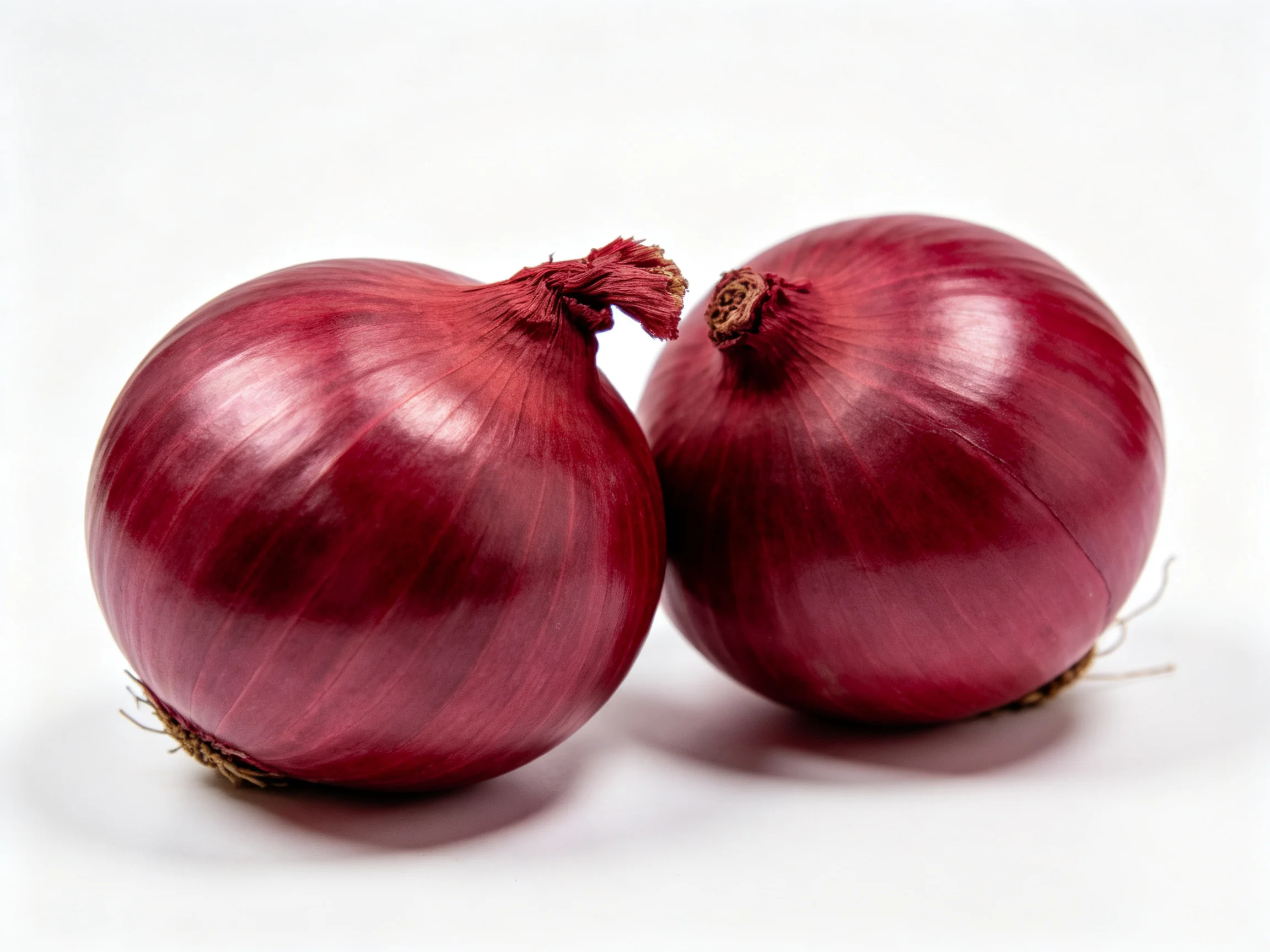 Two glossy red onions positioned closely on a white surface