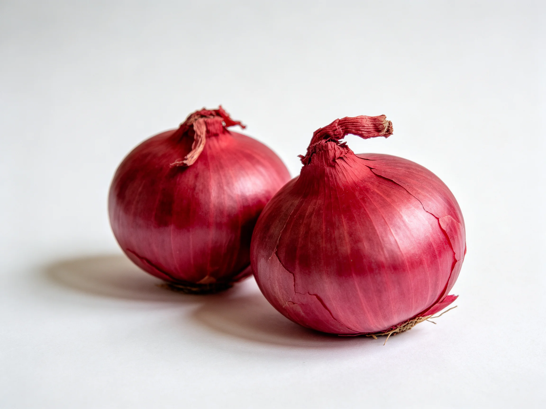 Two glossy red onions sit prominently on a stark white surface.