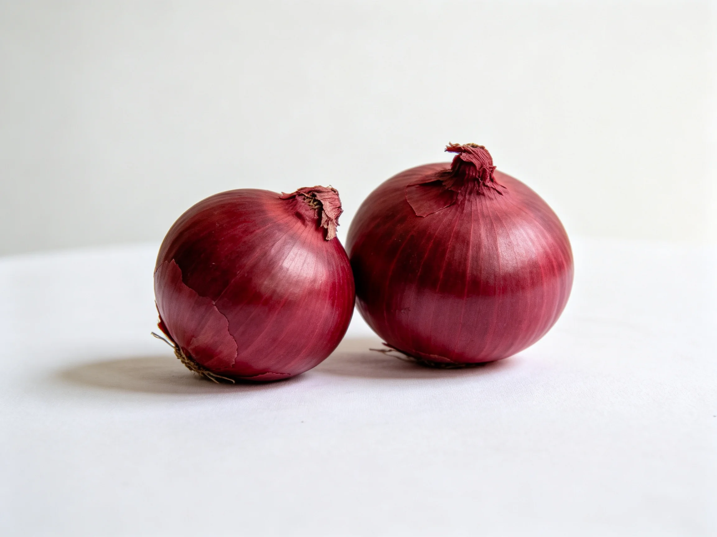Two glossy red onions sit side by side on a white surface
