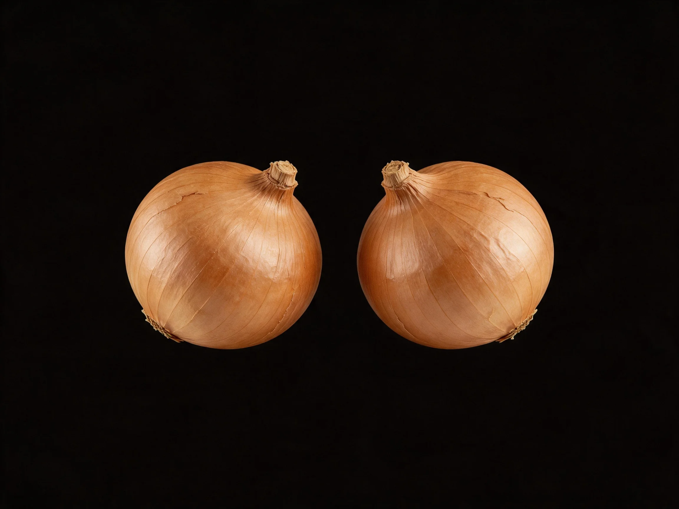 Two golden-brown onions positioned side by side on a black background