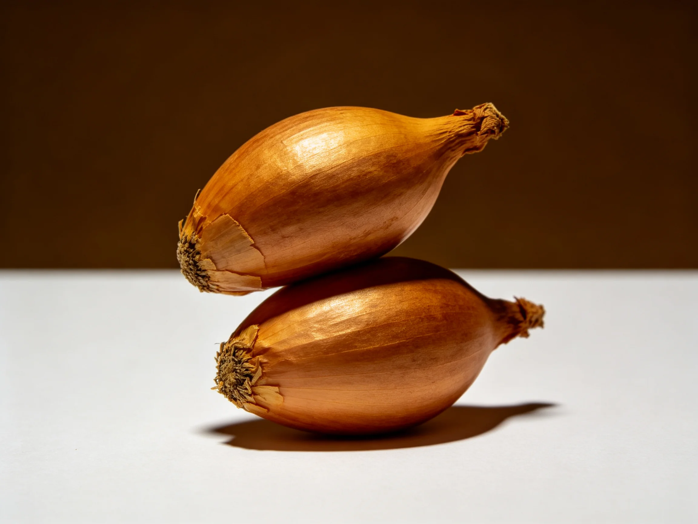 Two golden-brown shallots stacked on a white surface with a dark backdrop