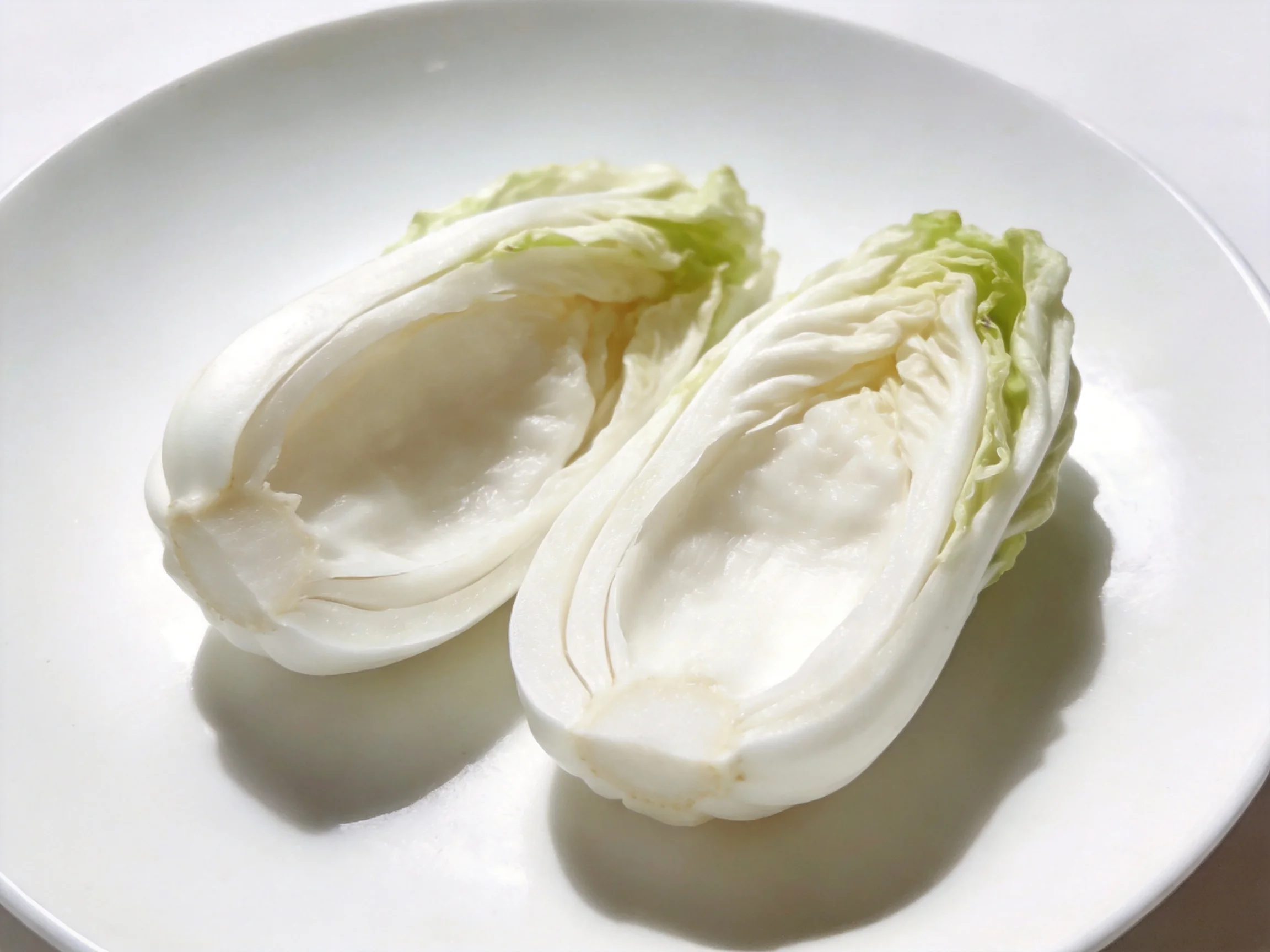 Two halved fresh napa cabbages on a plain white plate