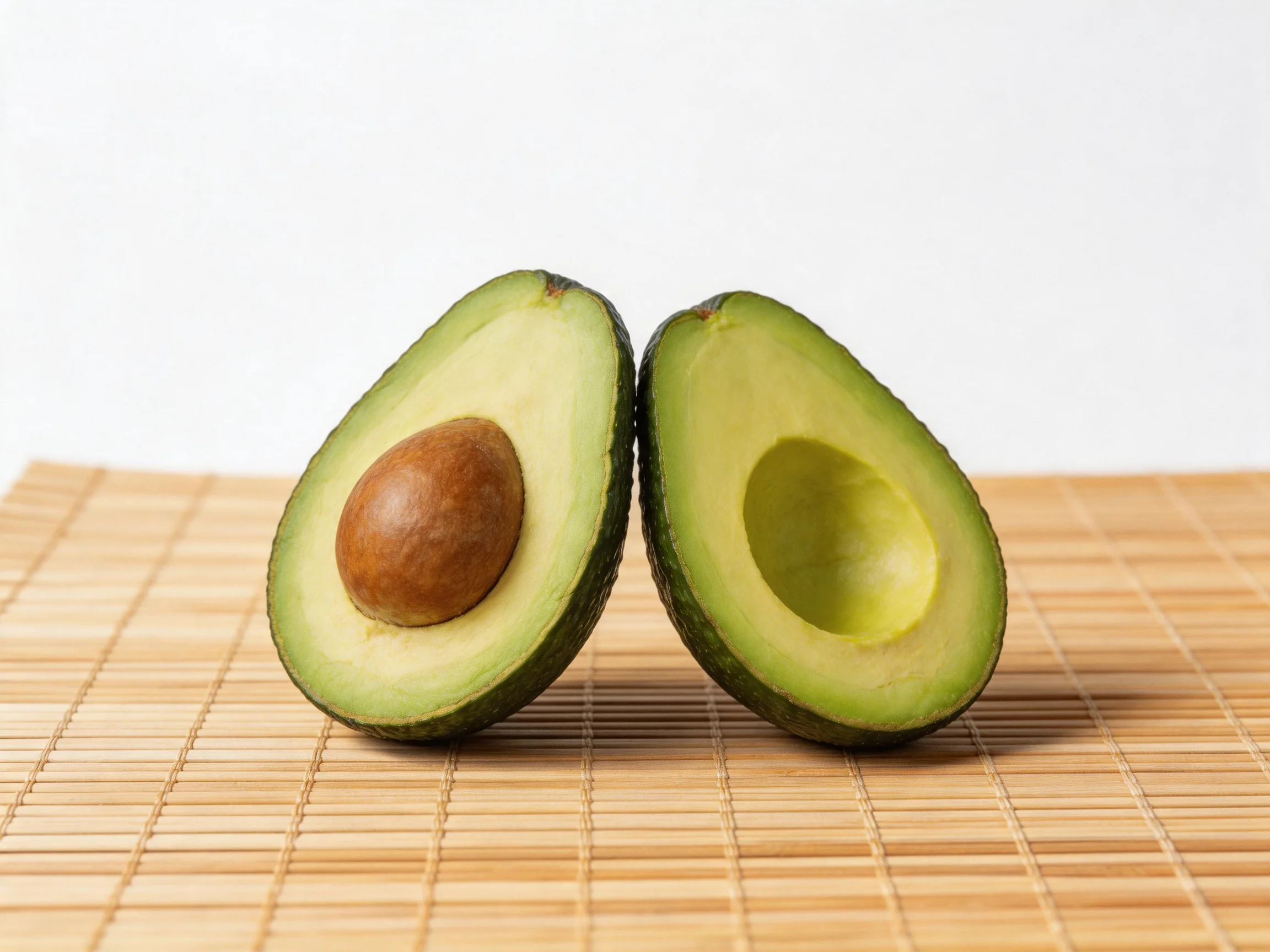 Two ripe avocado halves with brown seed on bamboo mat