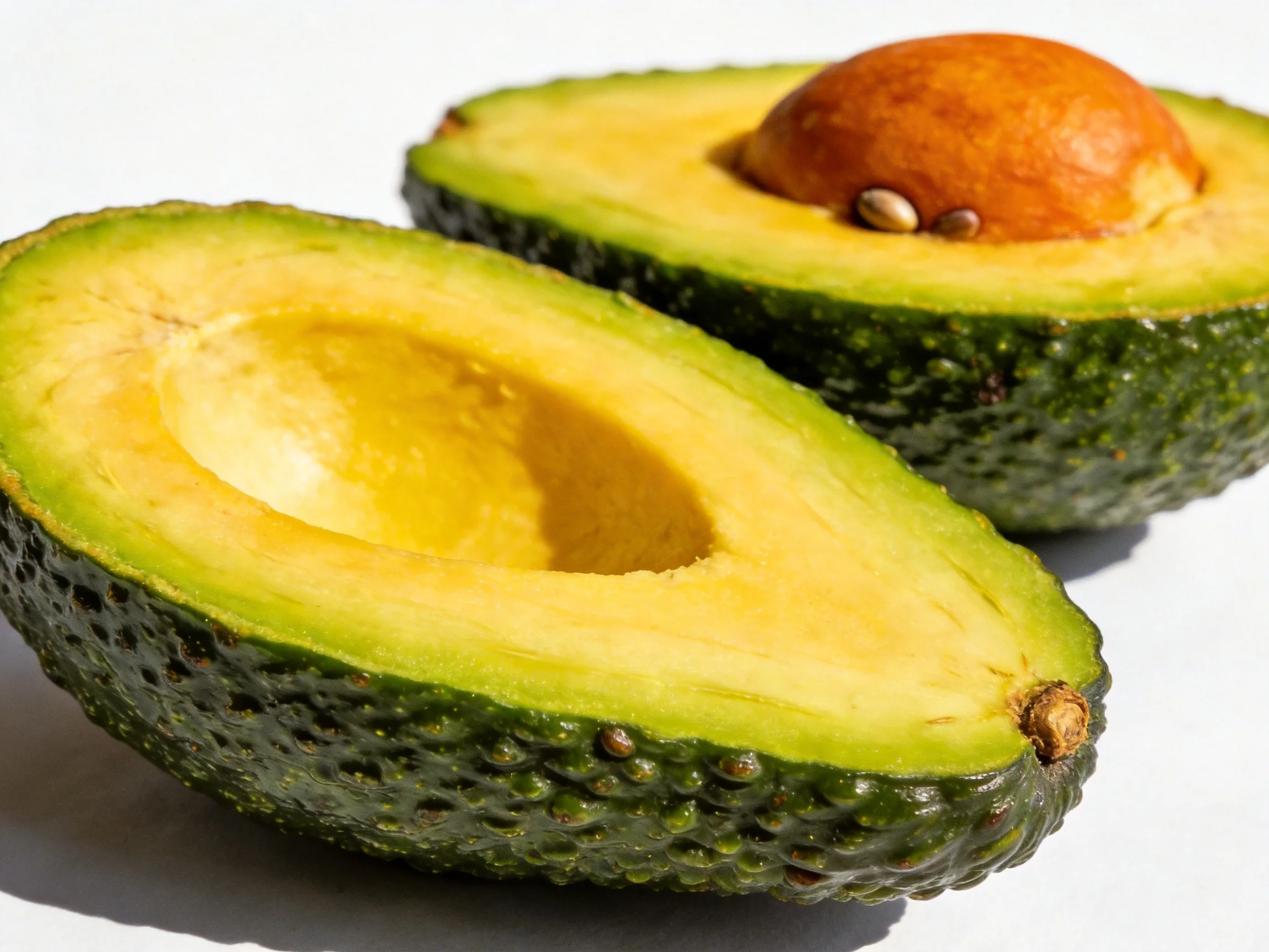 Two sliced avocados reveal yellow flesh and brown pits