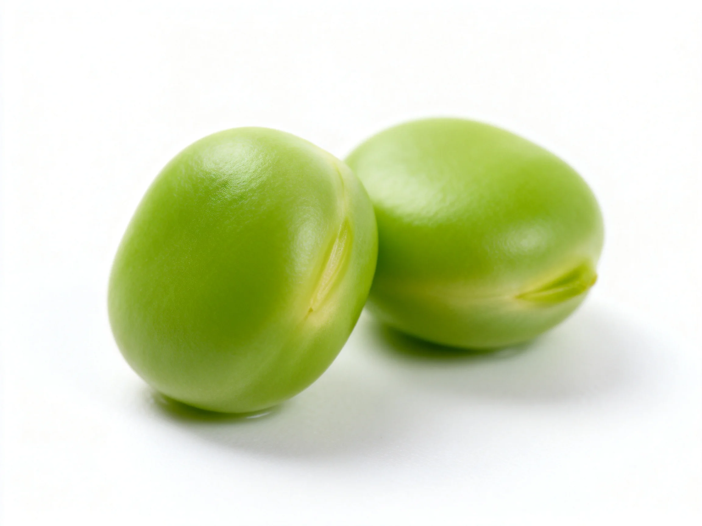 Two vibrant green peas nestled closely on a white surface