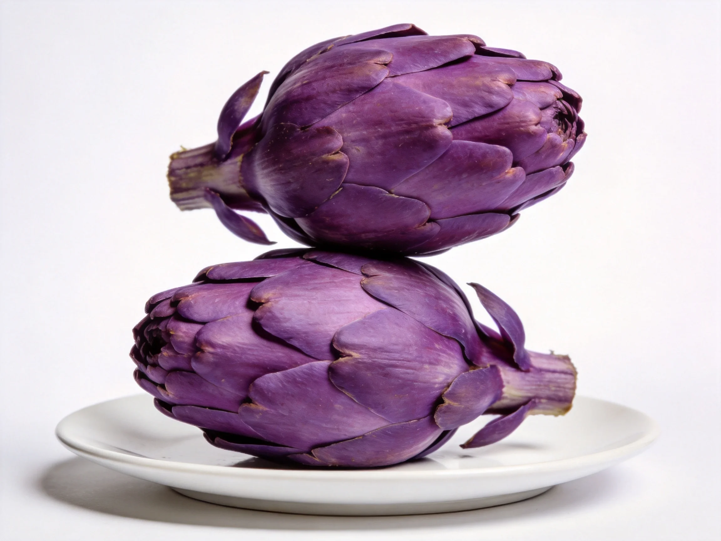 Two vibrant purple artichokes stacked on a white plate