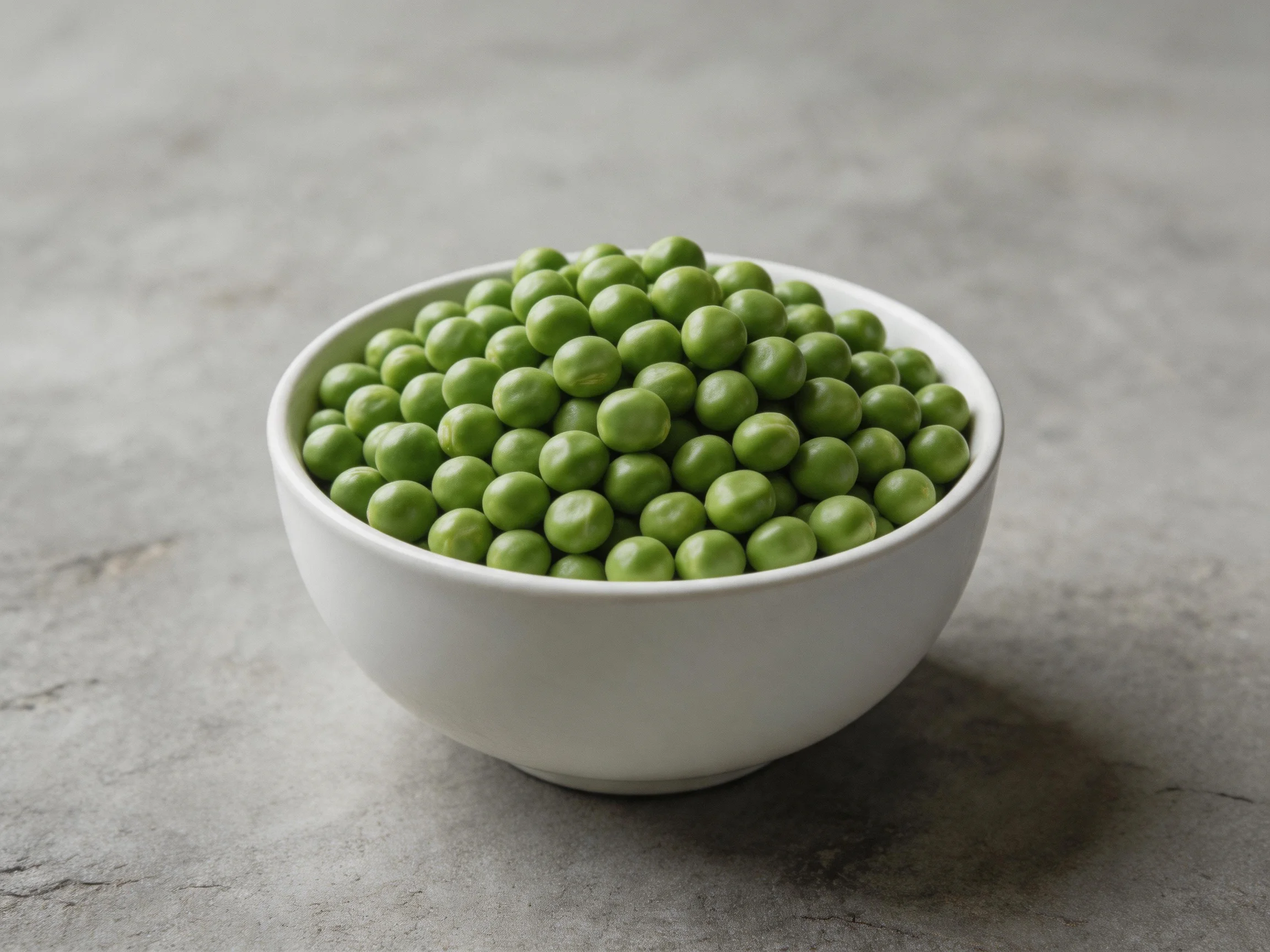 White ceramic bowl overflowing with fresh green peas on a gray surface