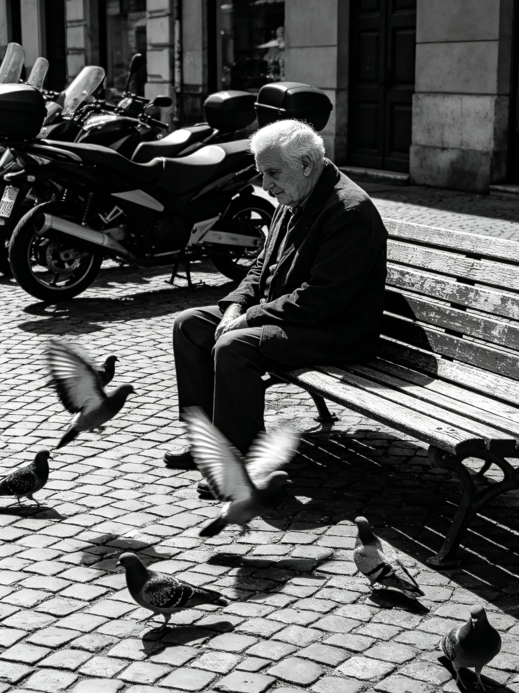An elderly man sits on a bench amid pigeons near parked motorcycles