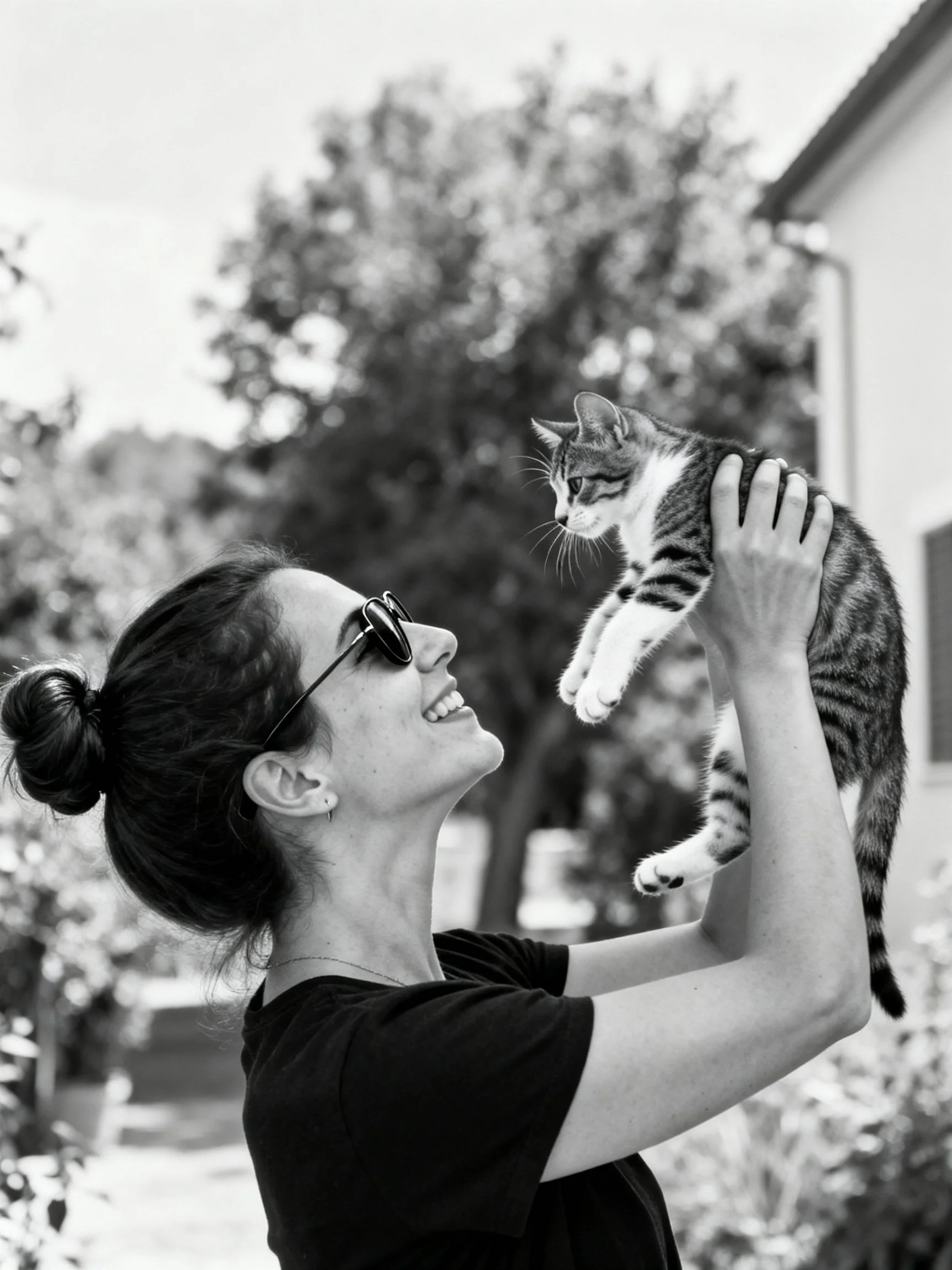 A woman lifting a tabby kitten in a monochrome outdoor setting
