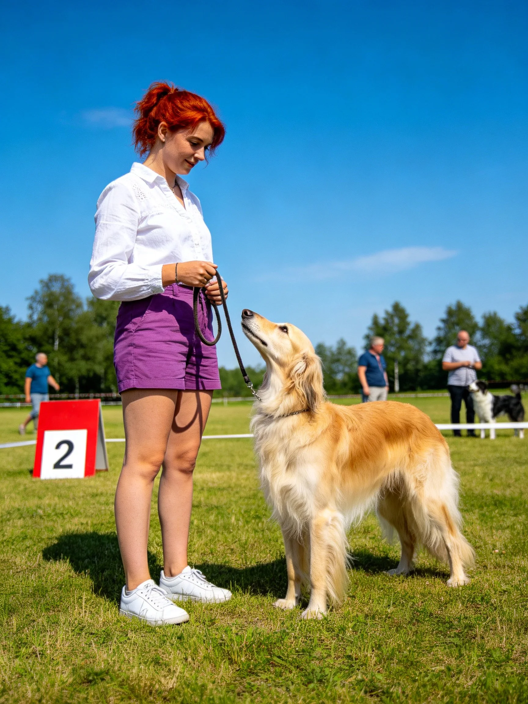 A red-haired woman stands with her golden retriever in a sunny field.