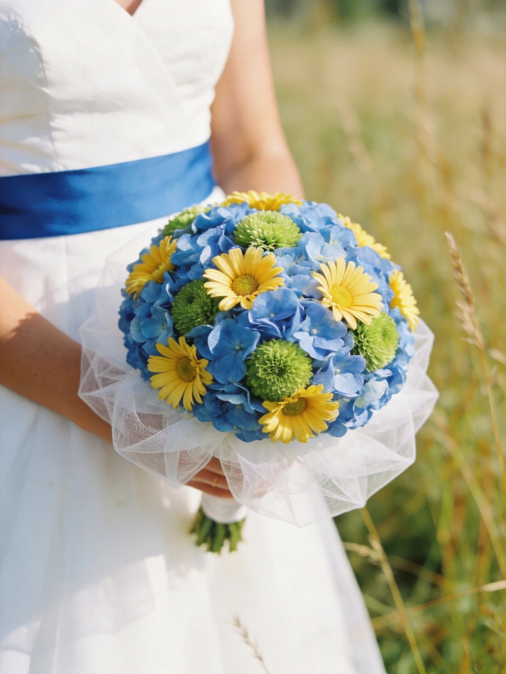A bride holds a colorful bouquet with blue, yellow, and green flowers