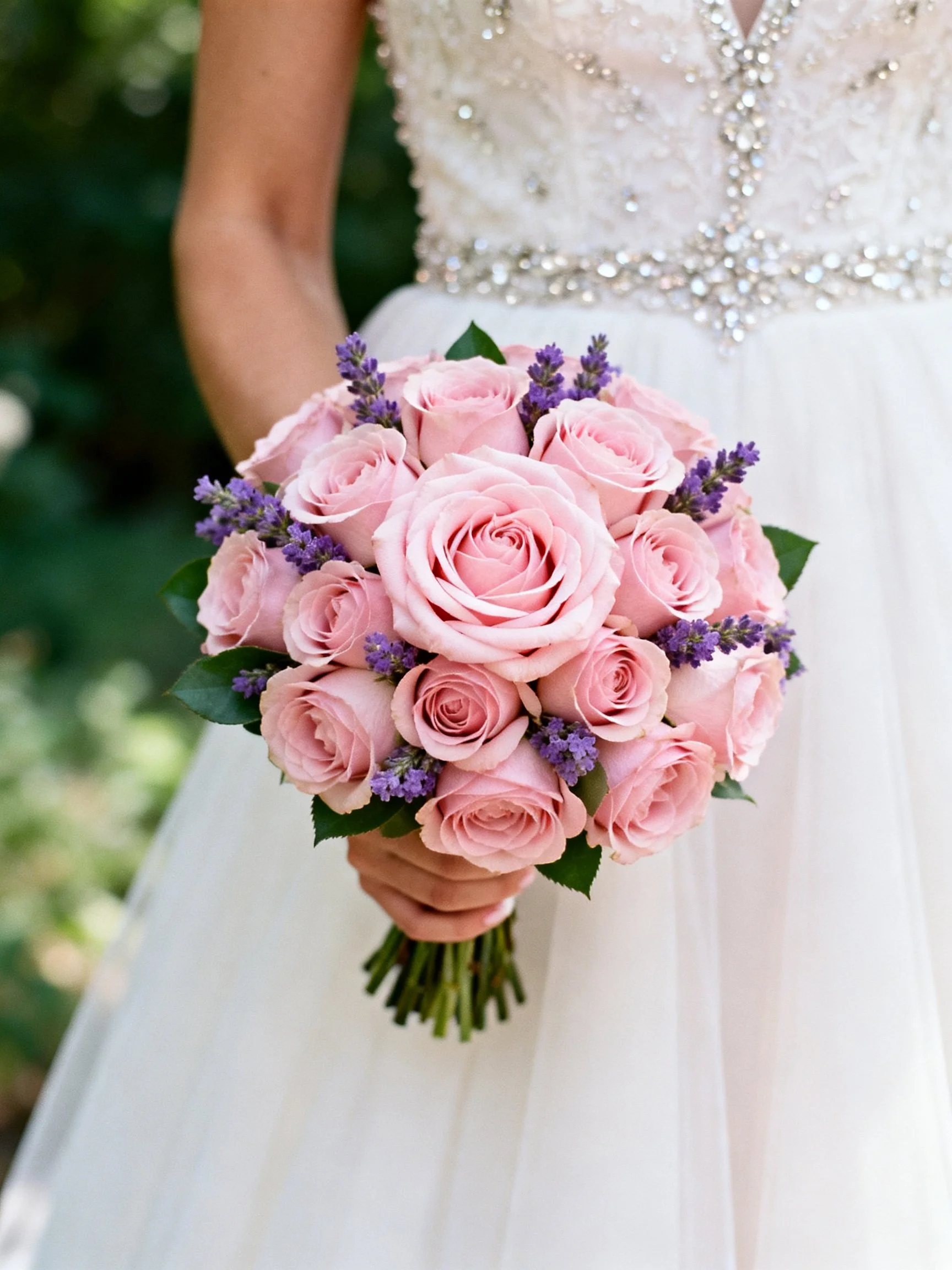 A bride holds a large pink rose bouquet with purple accents