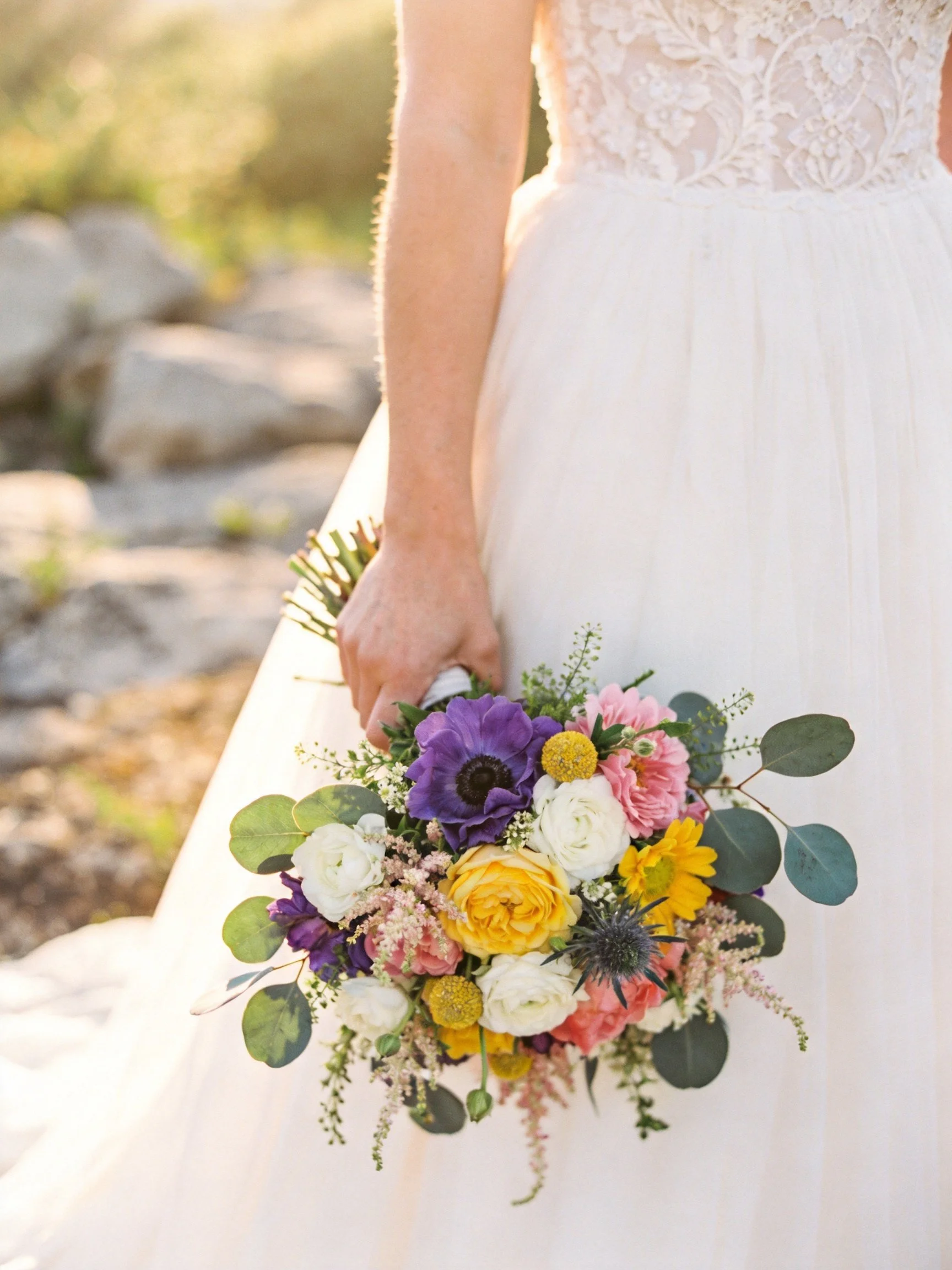 A bride holds a vibrant mixed flower bouquet with greenery