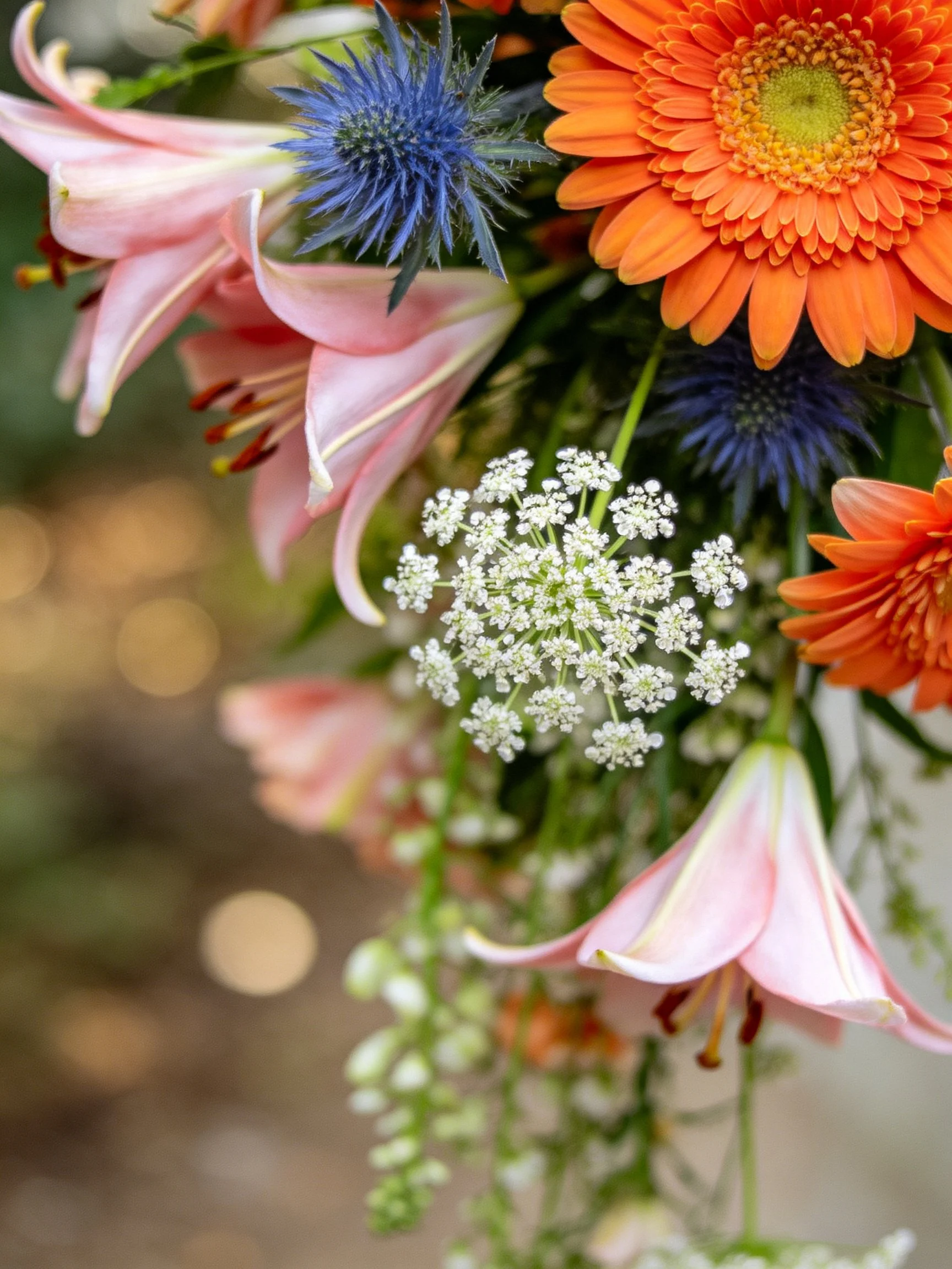 A vibrant bouquet with pink lilies, orange gerberas, blue thistles, and white blooms