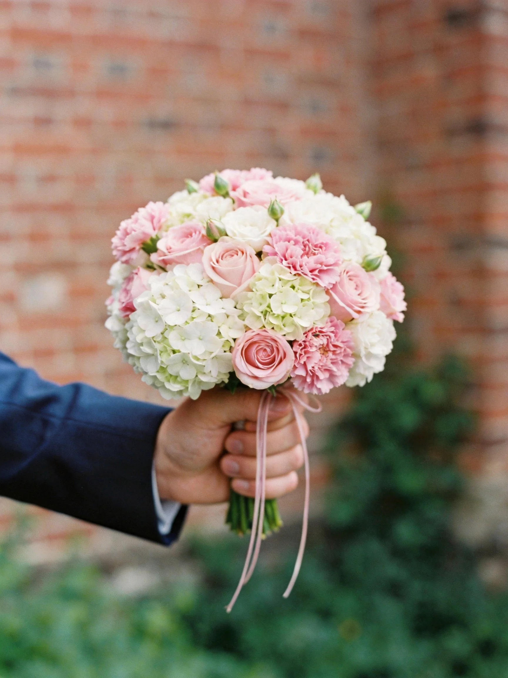 Hand holds a bouquet of pink roses, carnations, and white hydrangeas