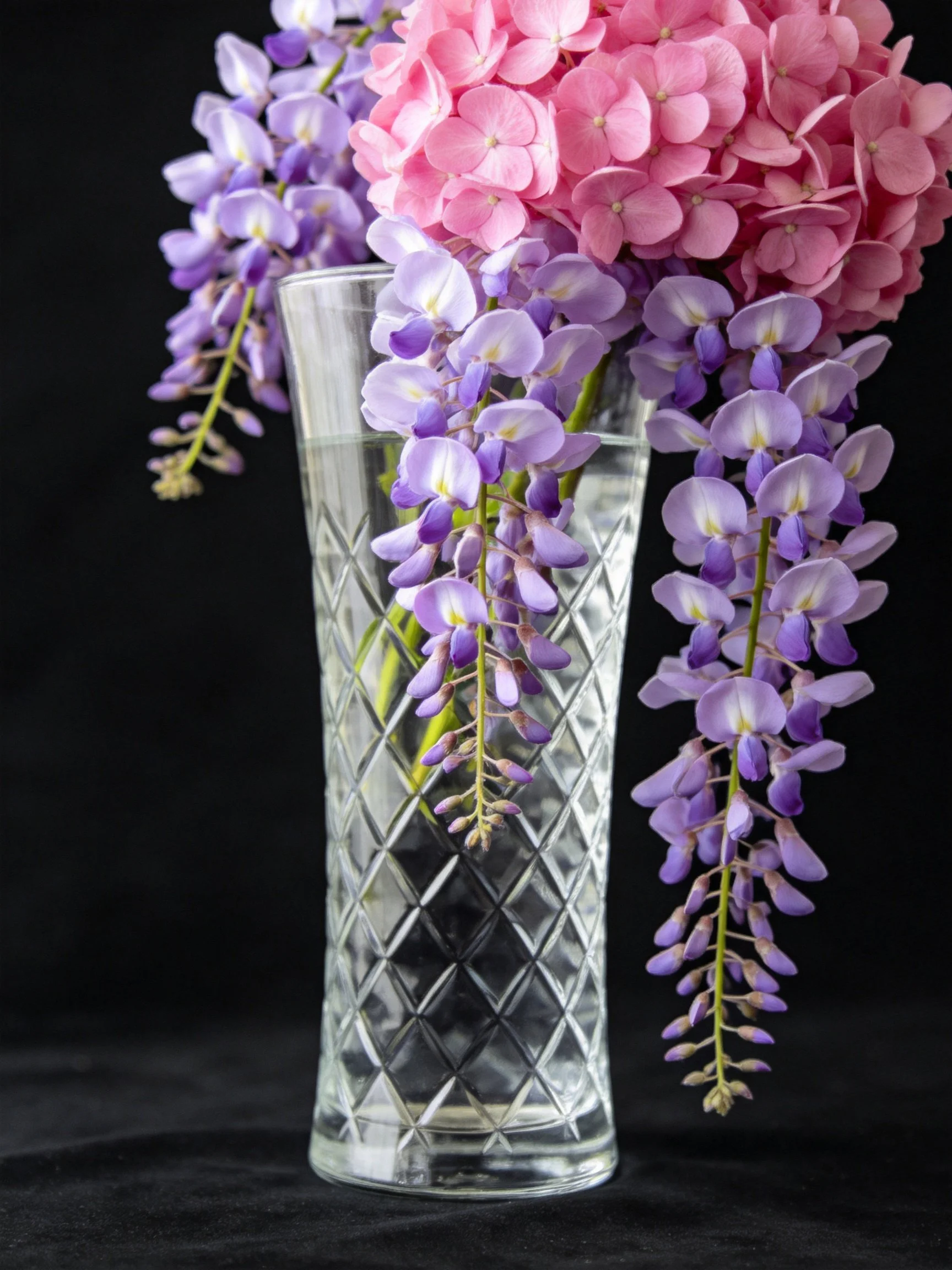 Pink hydrangeas and purple wisteria in a clear glass vase with water