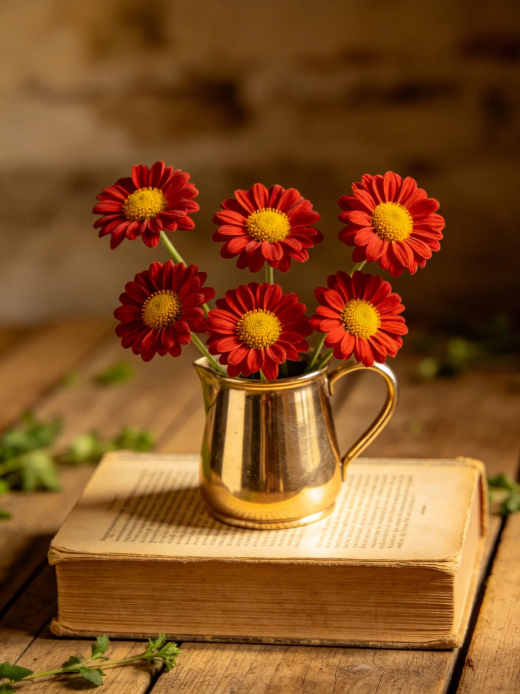 Six vibrant red flowers in a golden pitcher atop an aged book