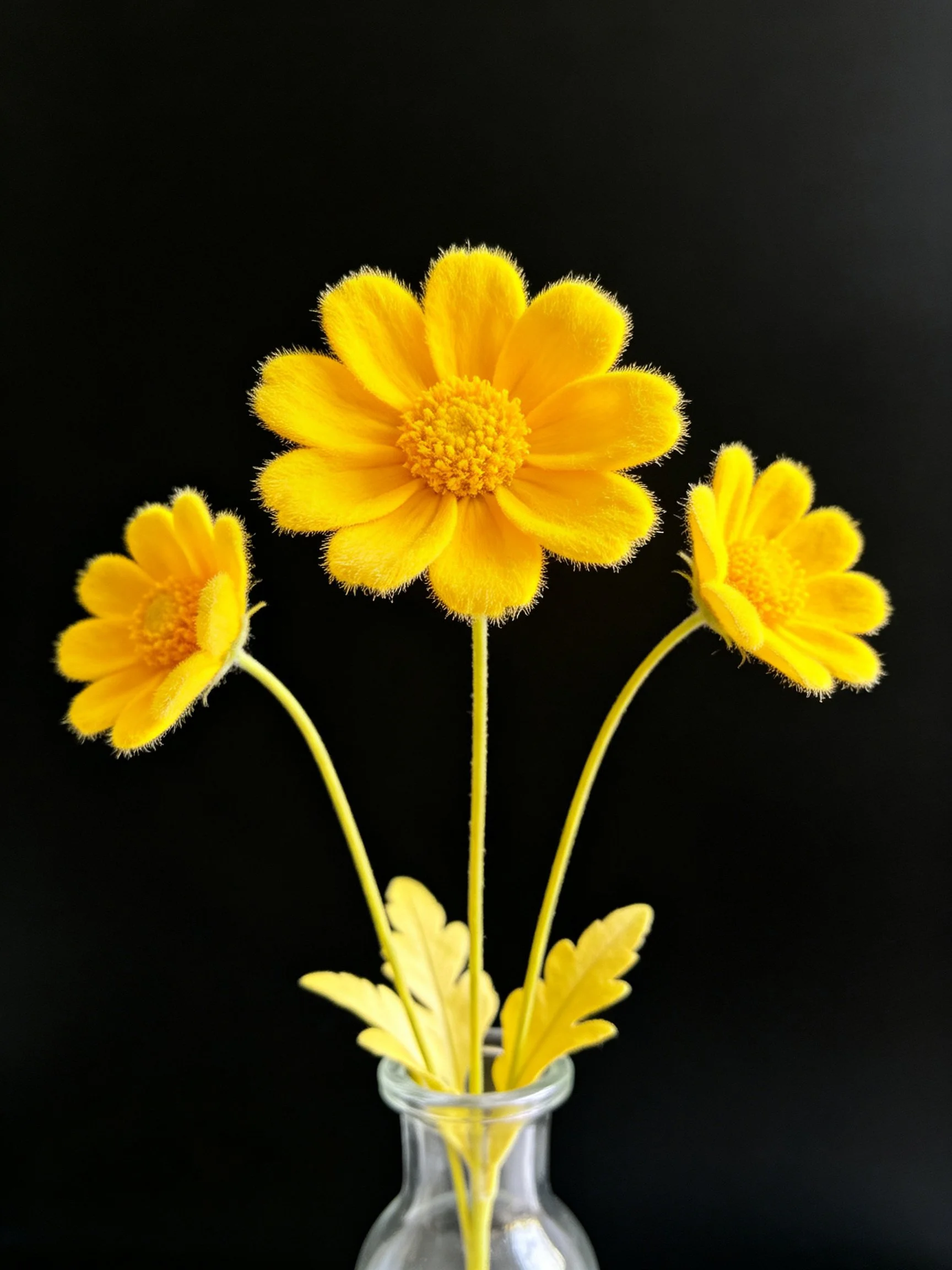 Three bright yellow felt flowers arranged in a clear glass vase