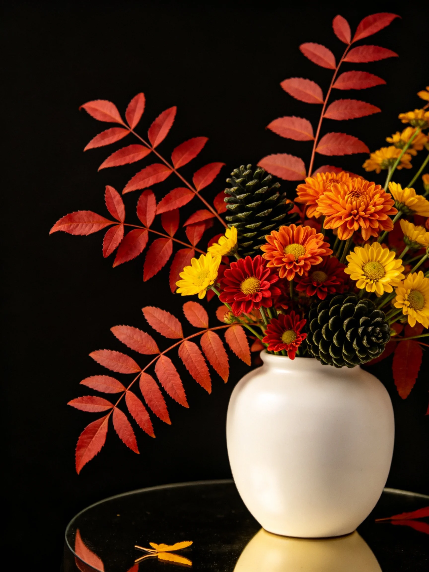 White vase with autumn floral display of red leaves, orange-yellow flowers, and pinecones