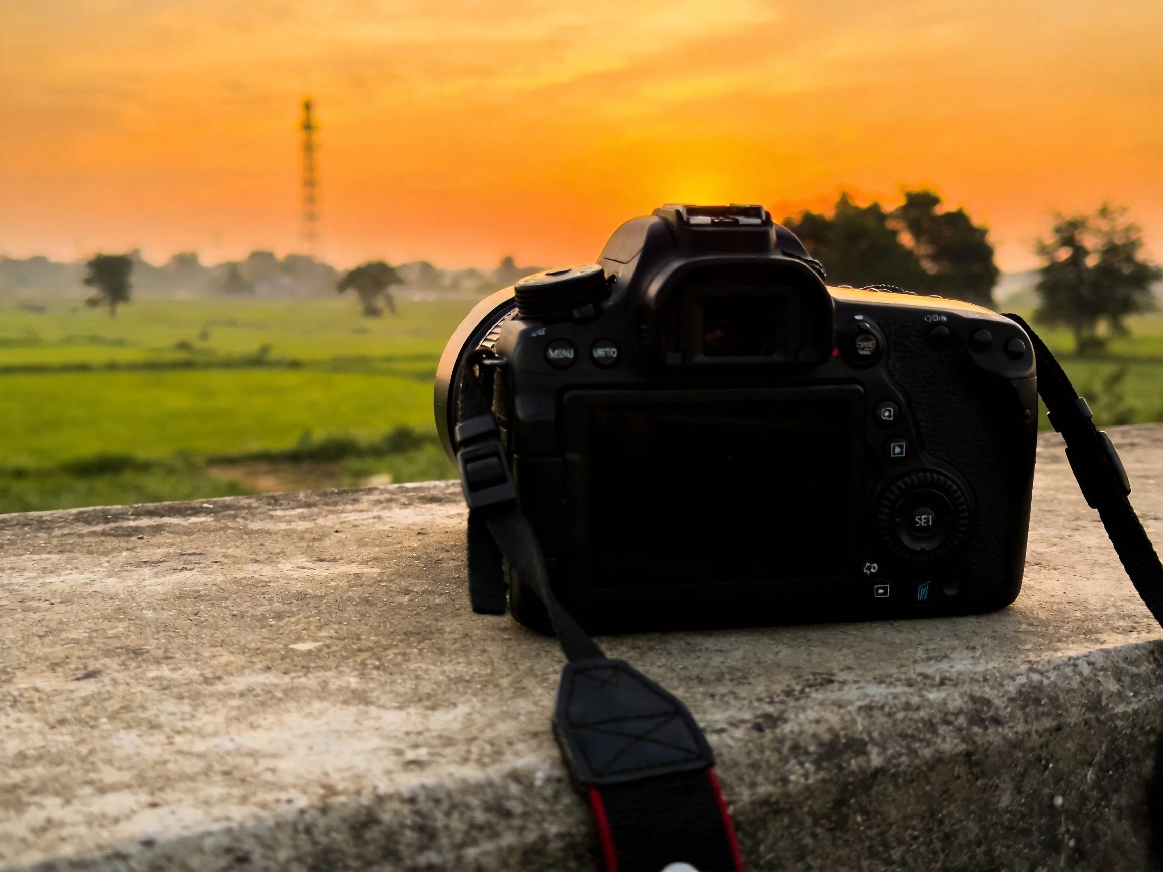 A DSLR Camera Rests on a Concrete Edge During a Golden Sunset Over Fields