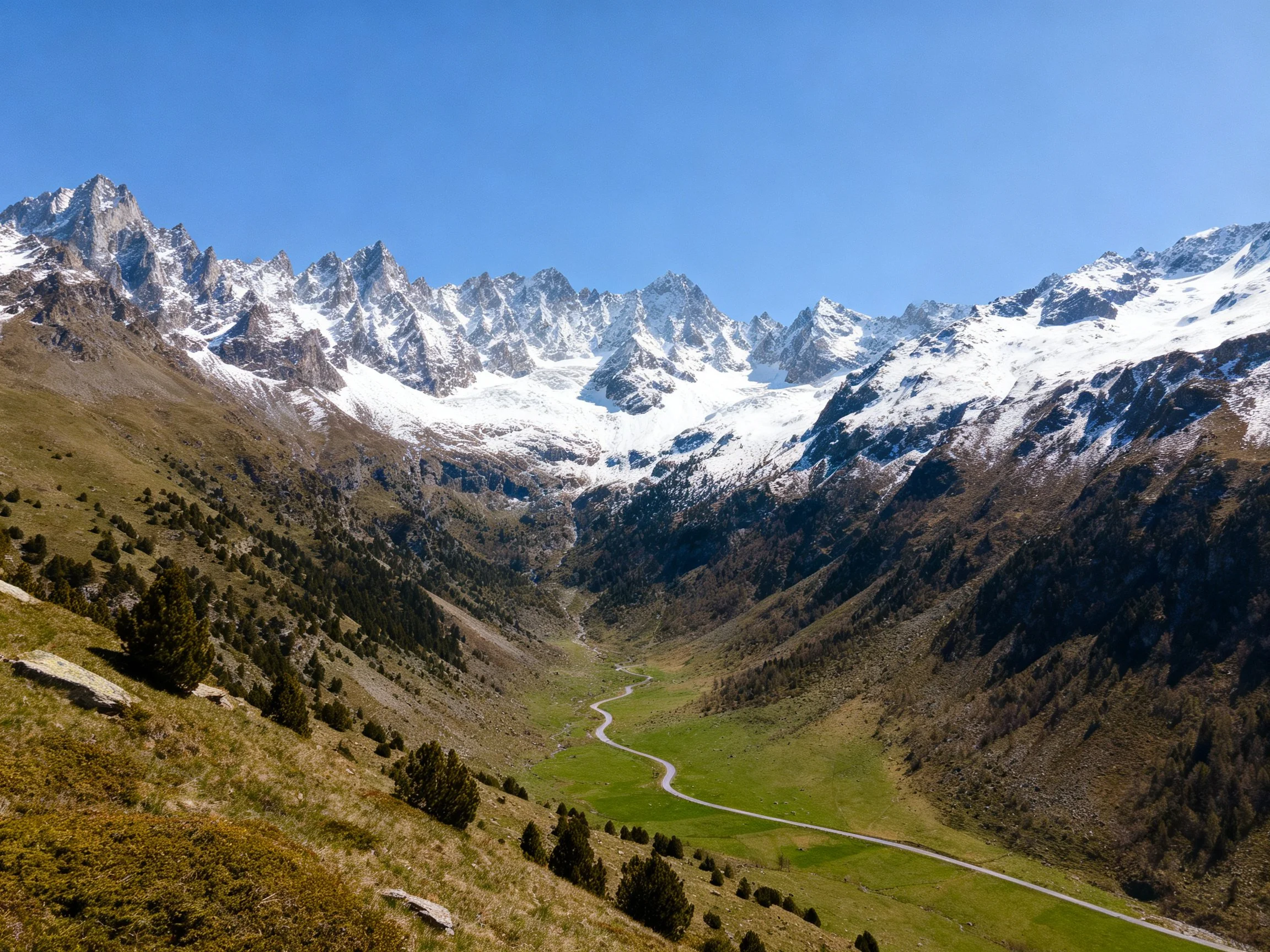 A Snow-Capped Mountain Valley With Green Pastures and Winding Road