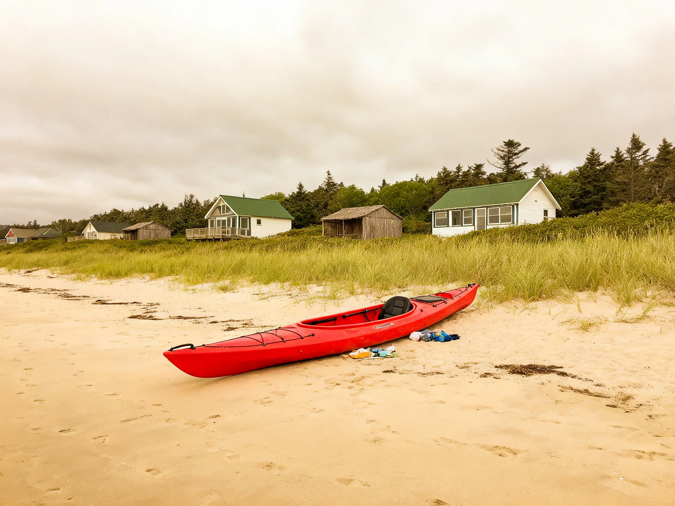 A bright red kayak rests on a sandy beach near green-roofed cottages
