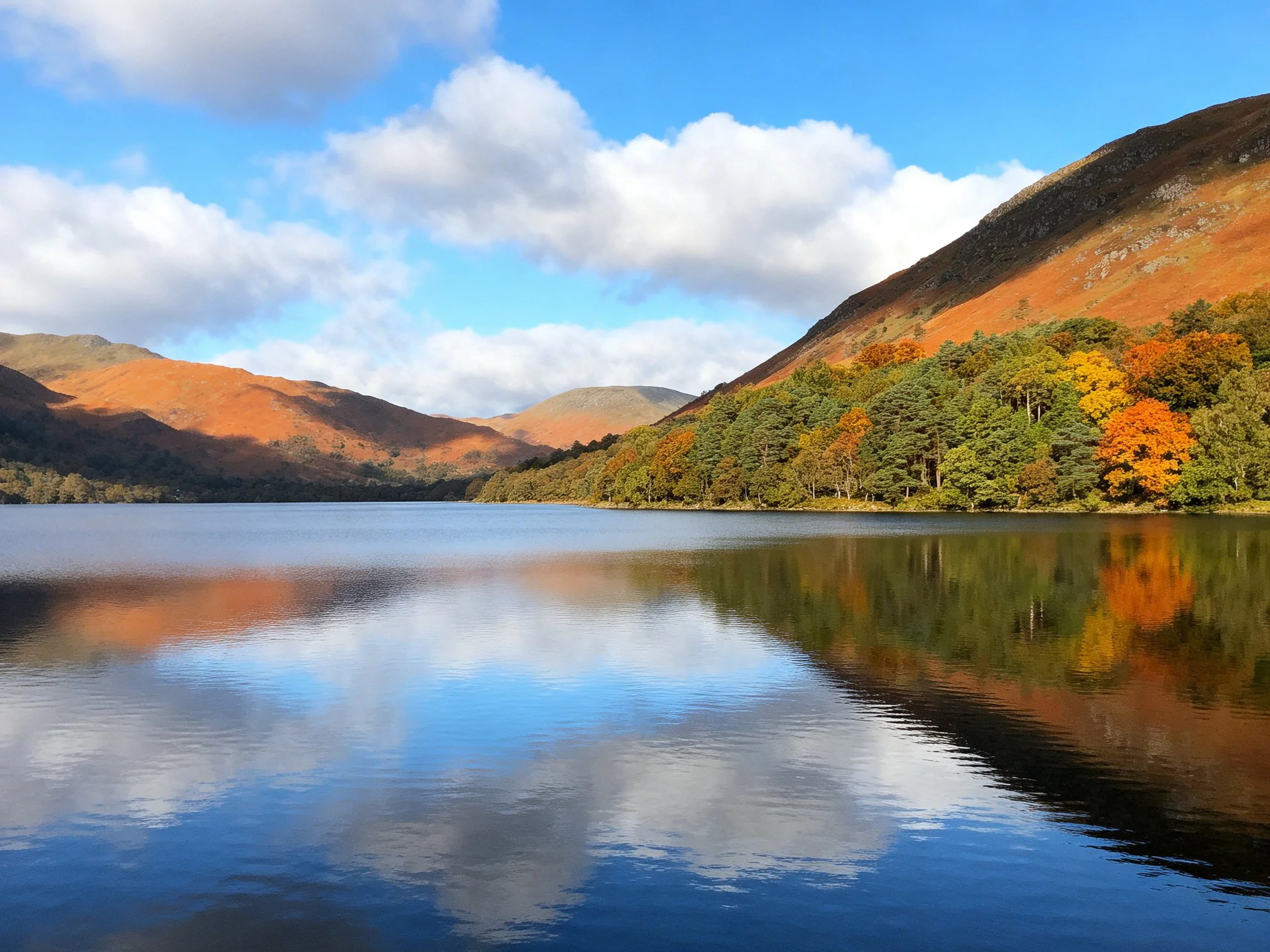 A calm lake reflects autumn-colored hills and vibrant trees