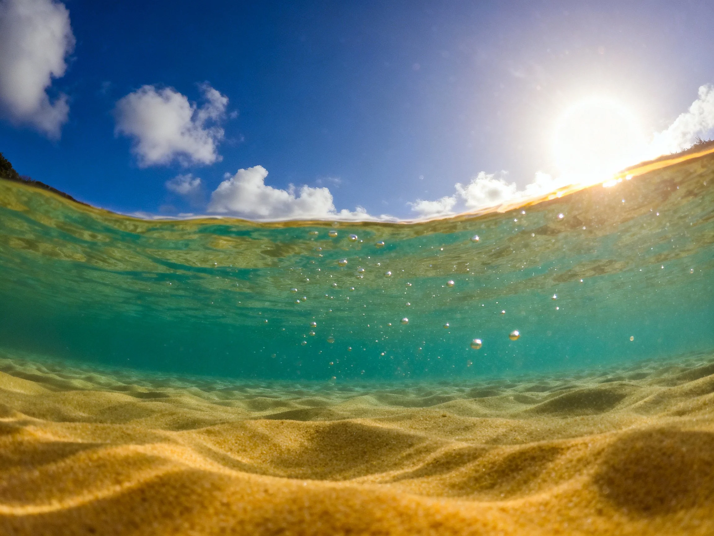 A clear turquoise underwater view with sandy ocean floor and sunny surface