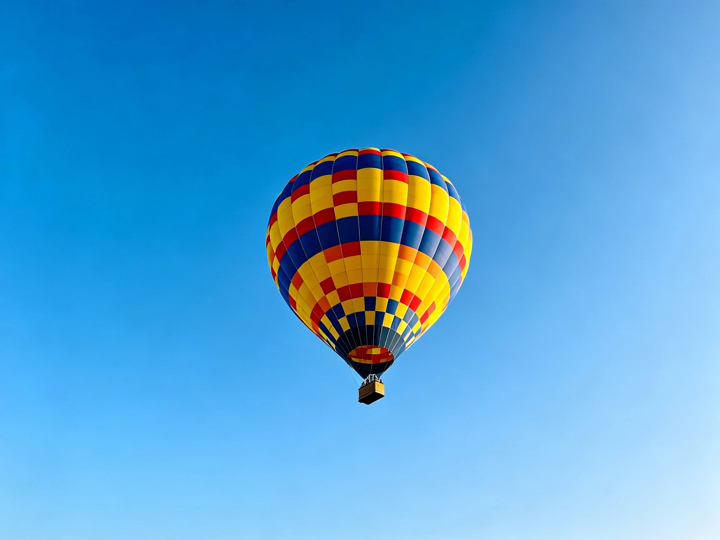 A colorful checkered hot air balloon floats against a clear blue sky
