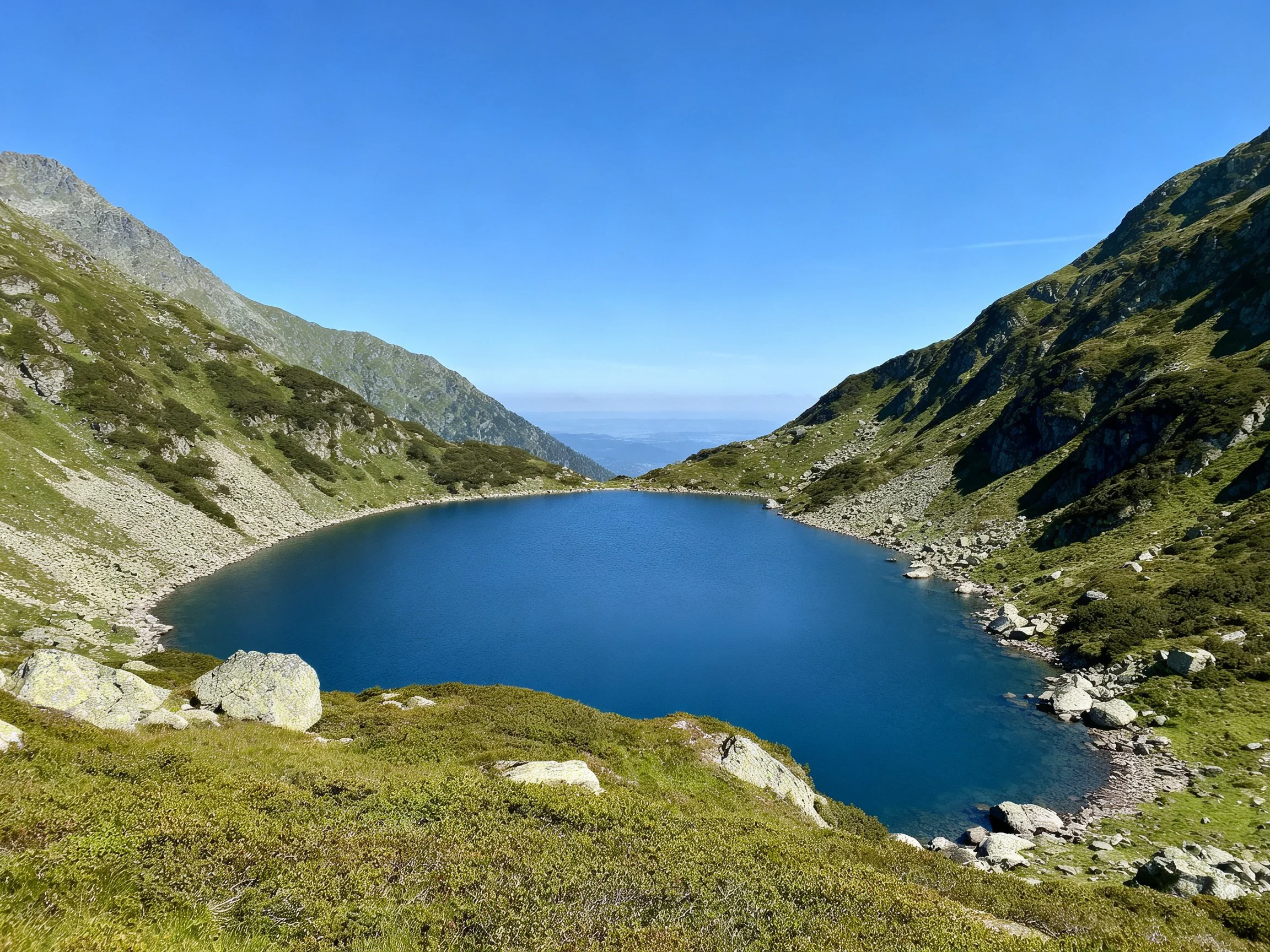 A deep blue alpine lake in a rocky green valley