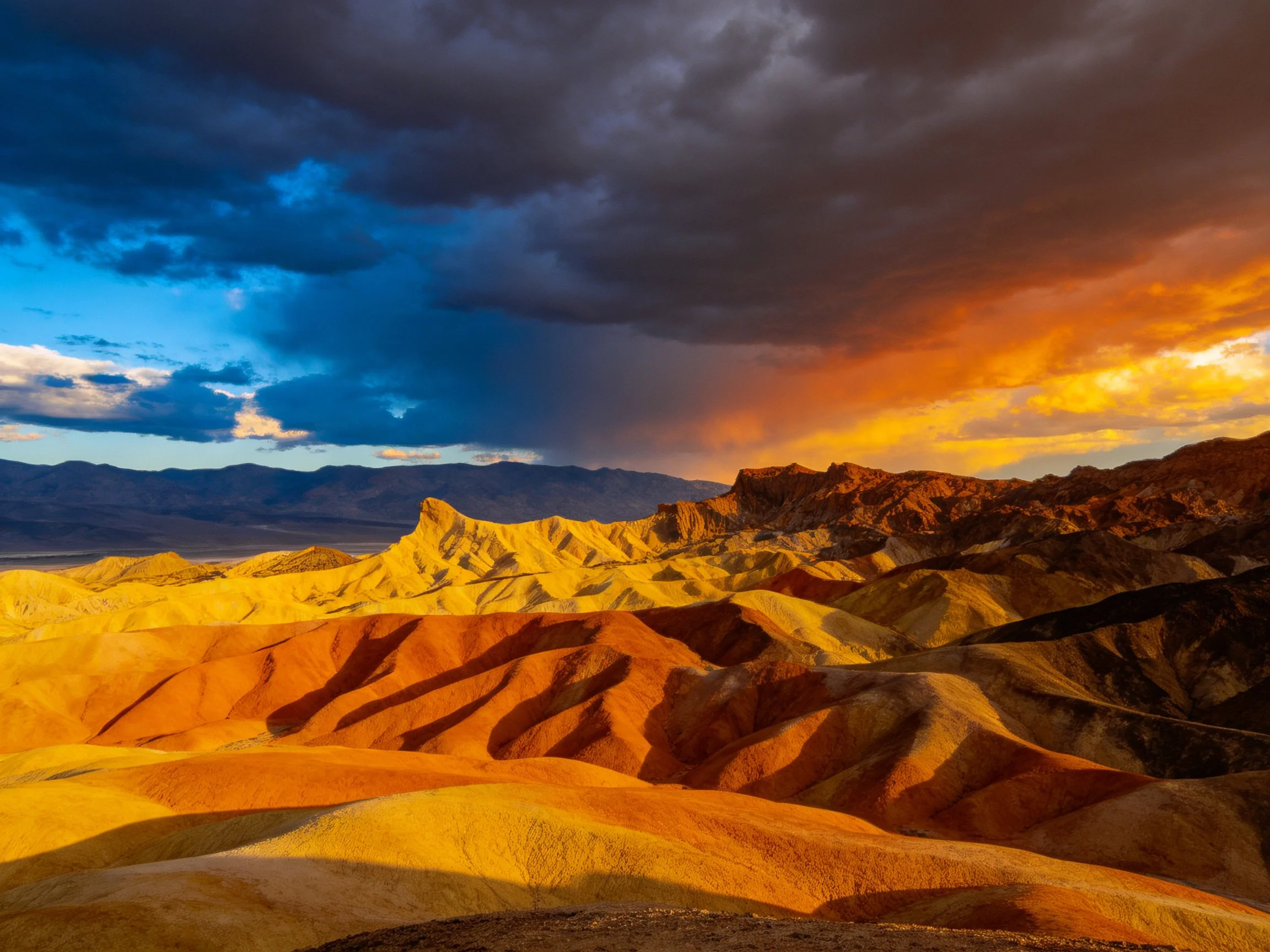 A dramatic desert landscape with multicolored mountain formations under contrasting skies