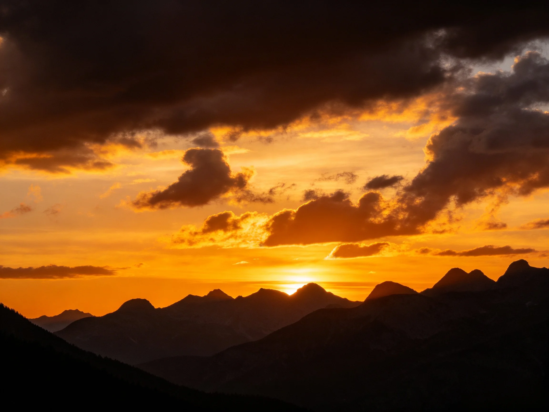 A dramatic sunset over mountain silhouettes with vibrant orange clouds