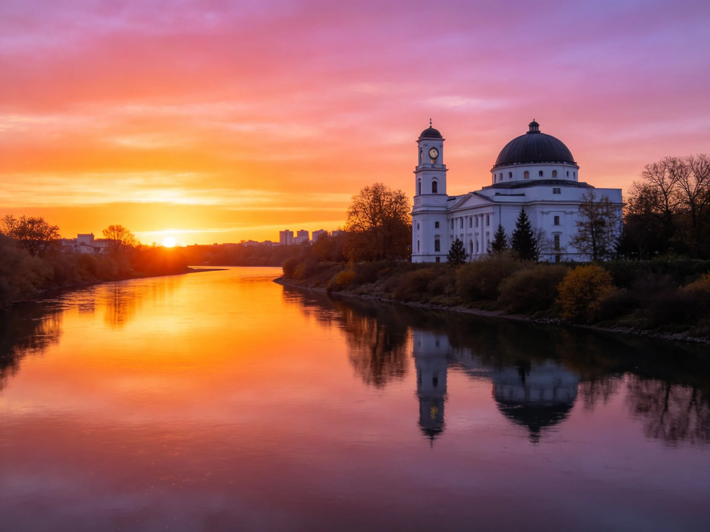 A grand white domed church beside a calm river at vibrant sunset