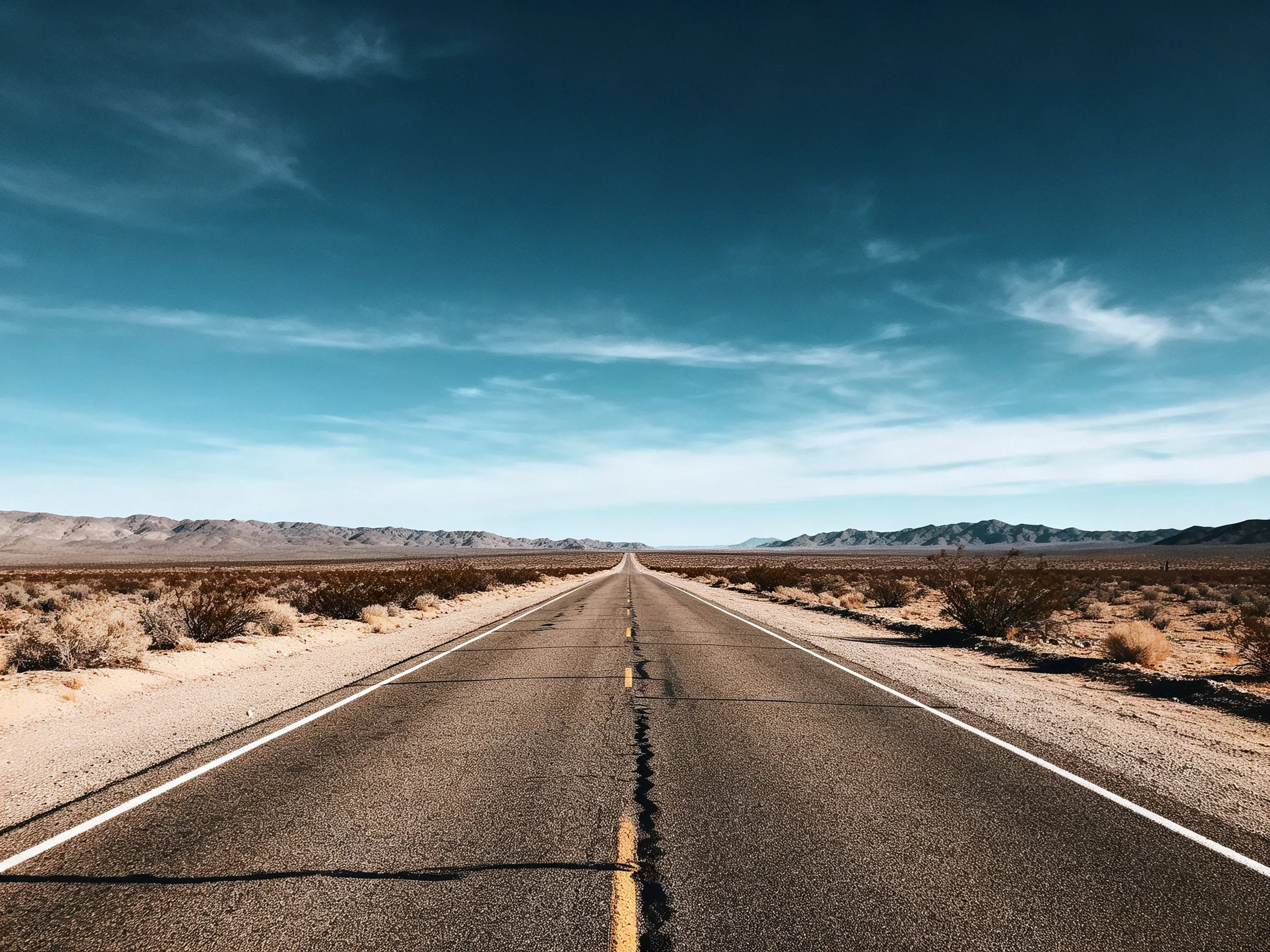 A long asphalt road stretches into a vast desert with distant mountains