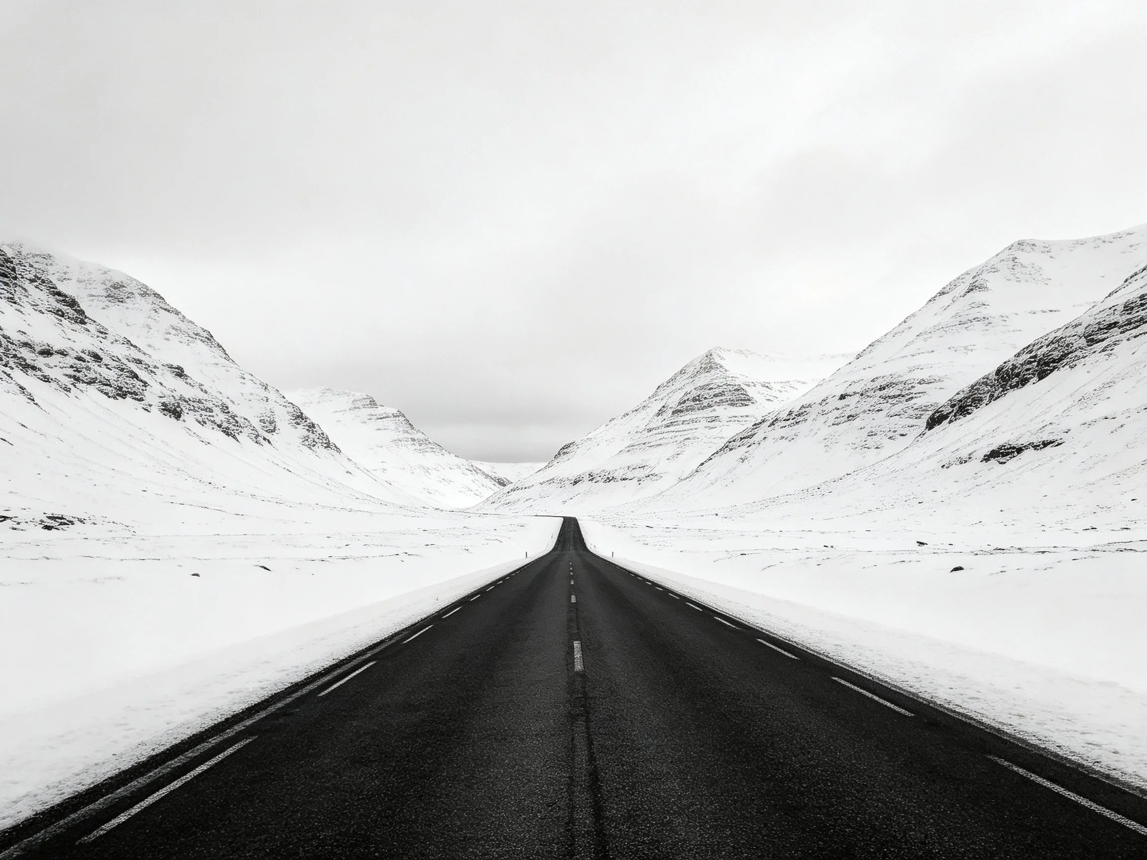 A long dark road stretches between snow-draped mountain ridges
