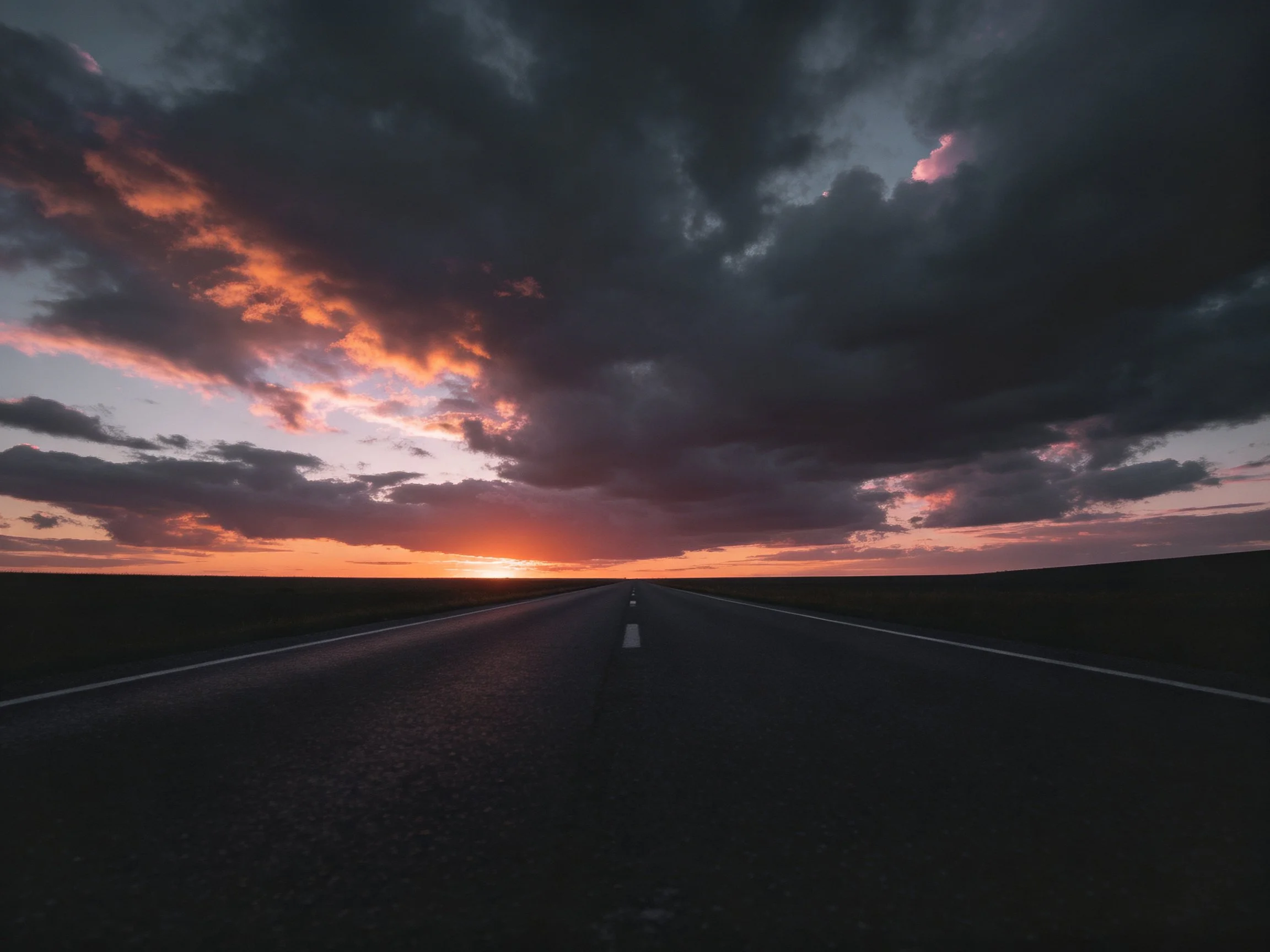 A long road under dark stormy skies with vivid sunset hues