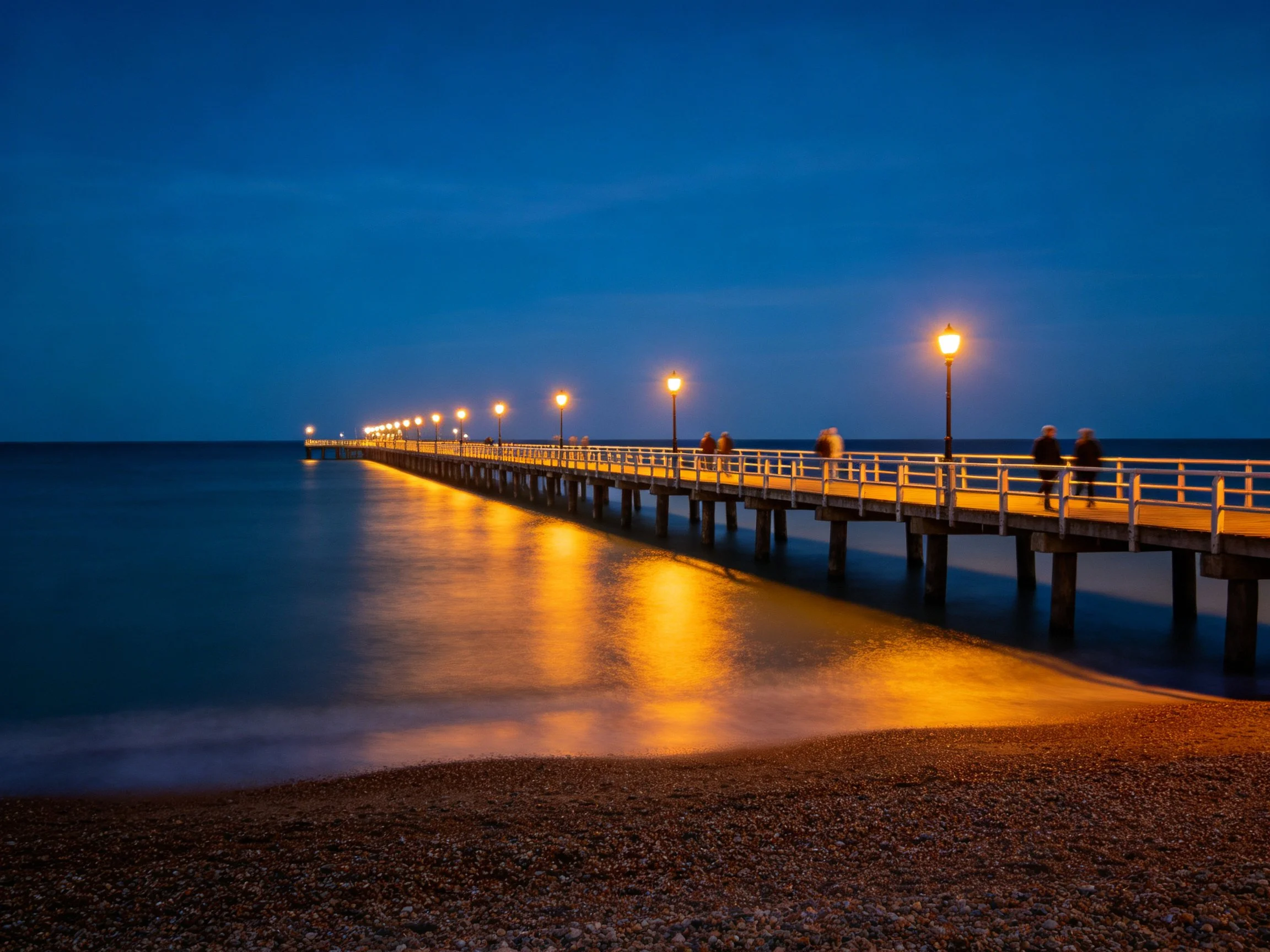 A long wooden pier illuminated by golden lamps over calm blue waters