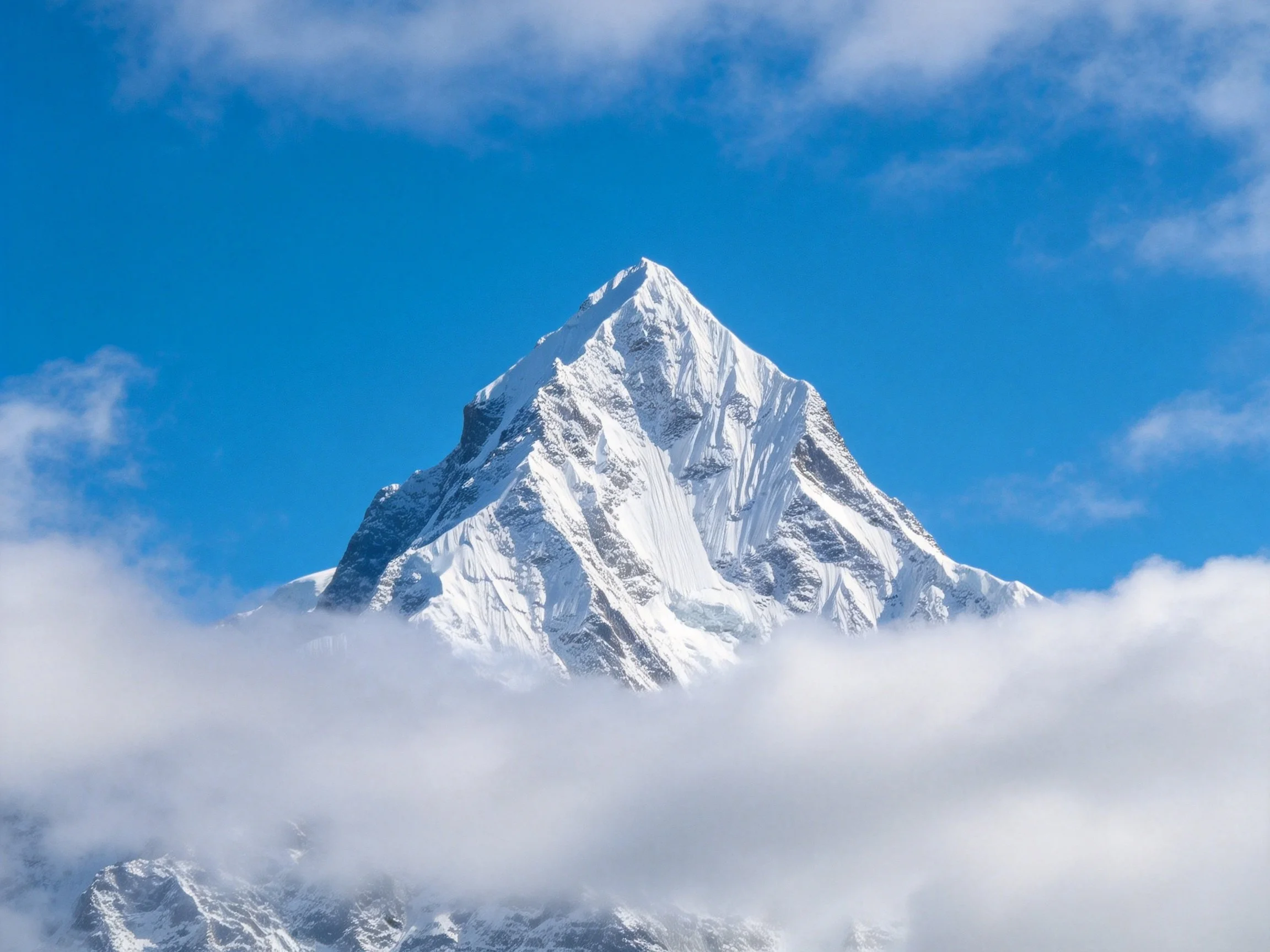A majestic snow - capped peak rises against a bright blue sky with scattered clouds