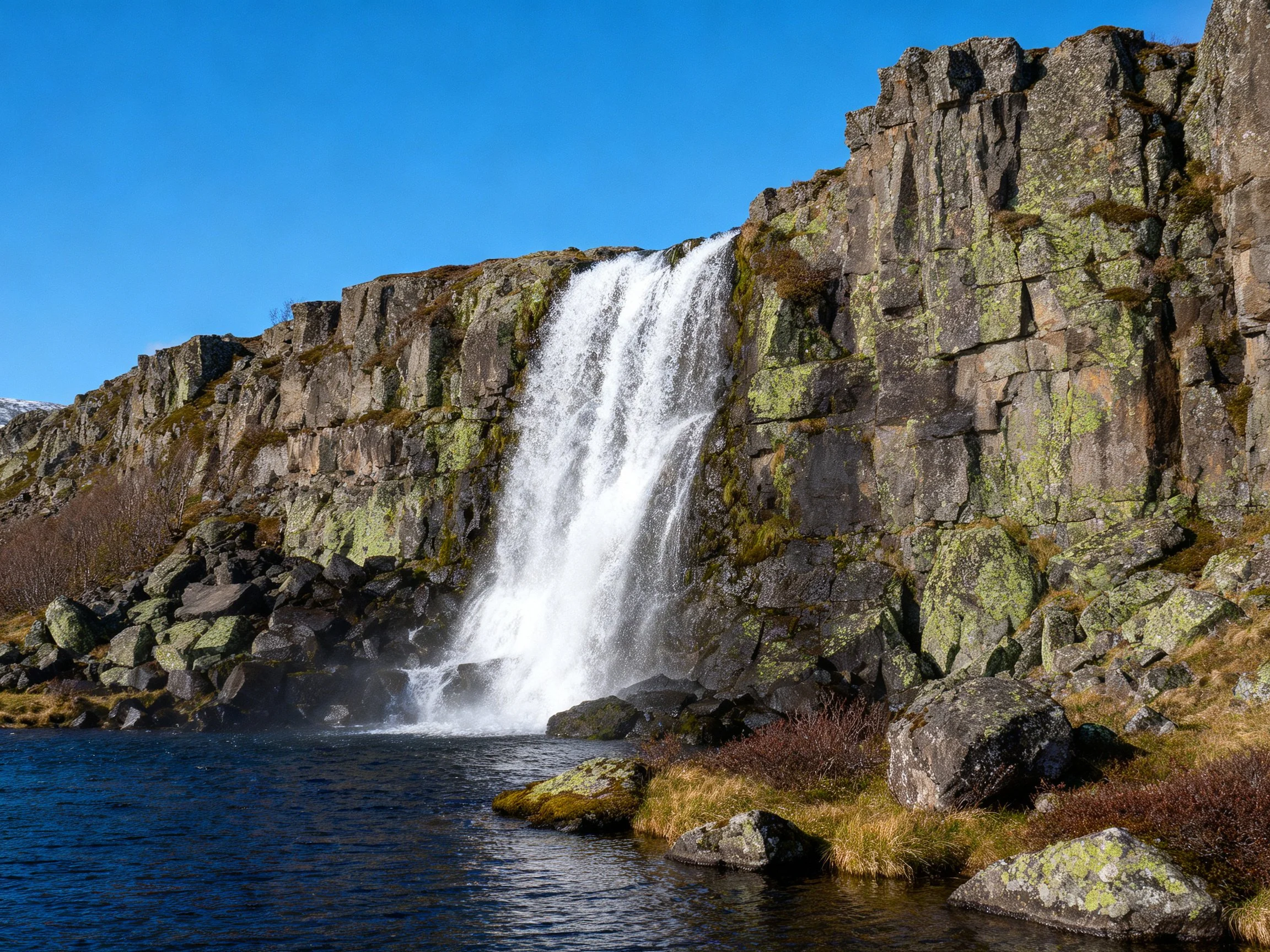 A majestic waterfall cascades over moss-covered rocky cliffs into a deep pool